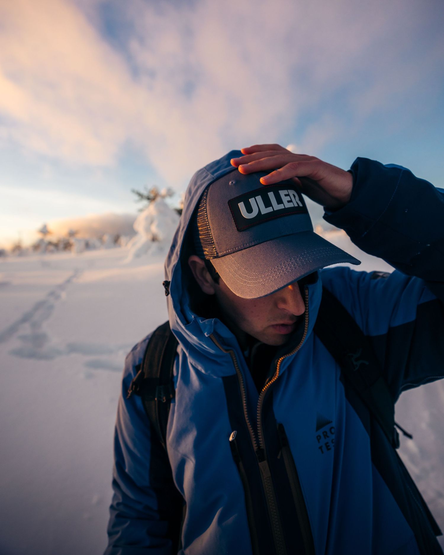 Silhouette of person adjusting baseball cap against sunset sky.