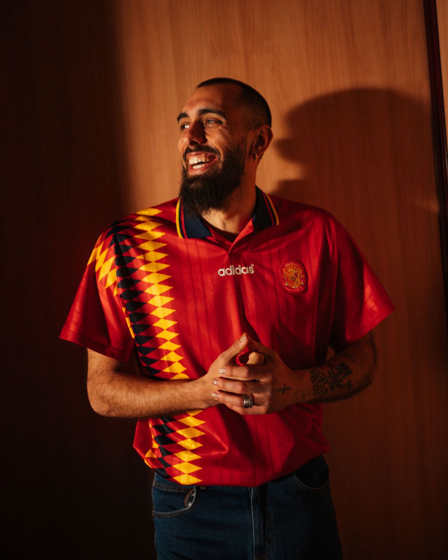 Smiling man with beard wearing a red Adidas Spain retro football jersey with geometric pattern.