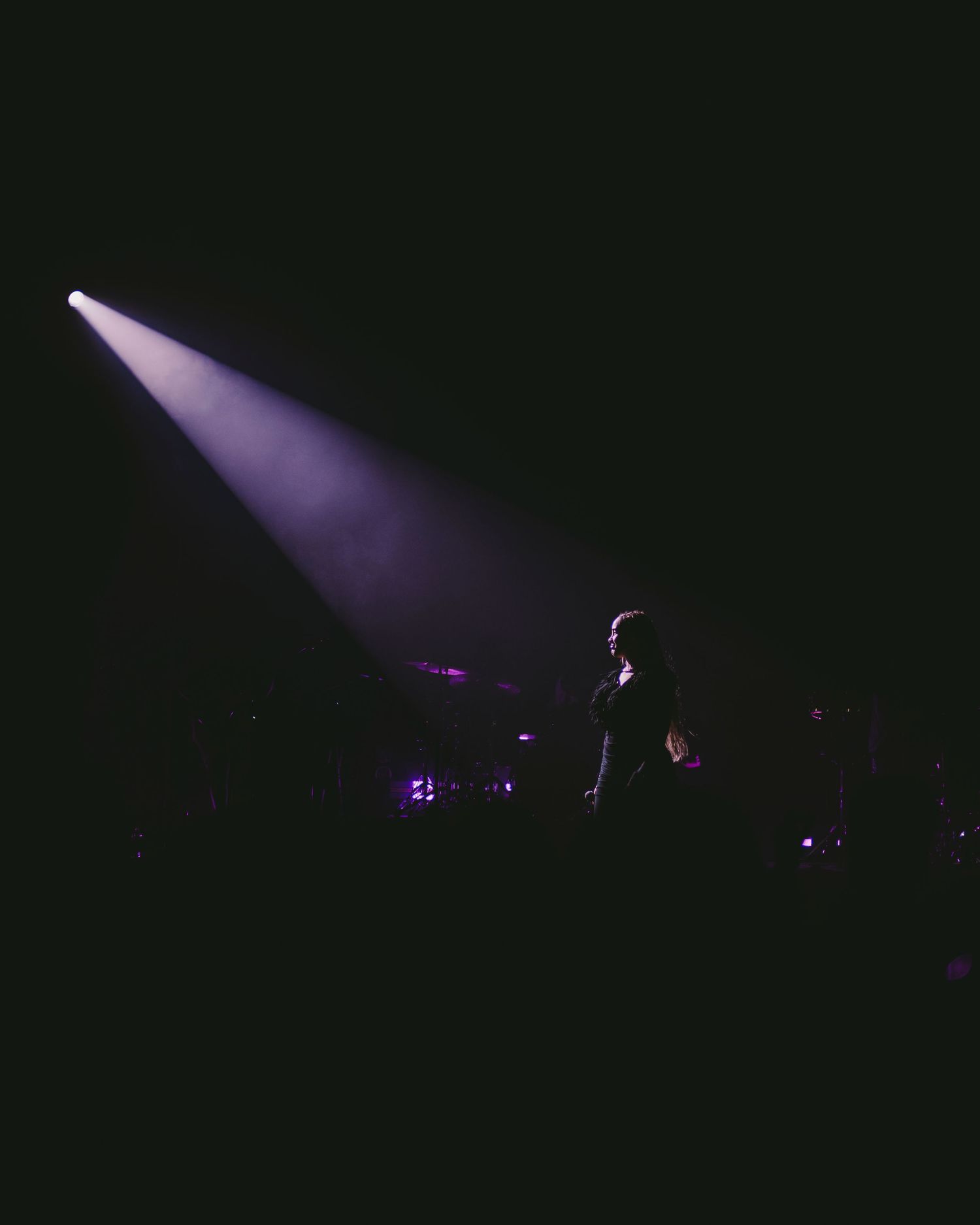 Dramatic stage performance silhouette under single purple spotlight beam.