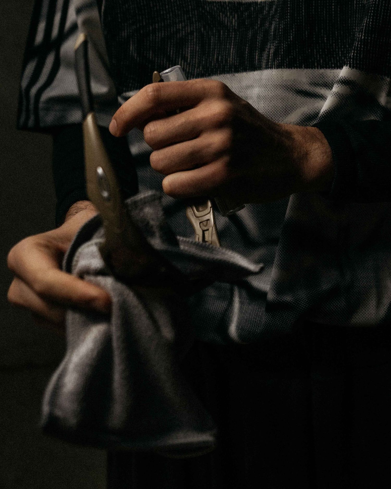 Close-up of hands holding a knife and pliers wrapped in a gray cloth apron.