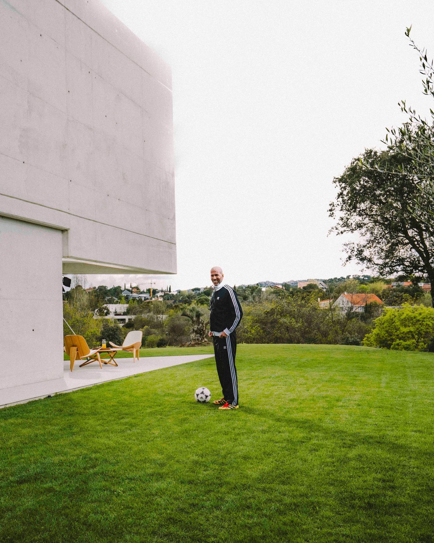 Person playing soccer on a grassy lawn next to a modern white building on an overcast day.