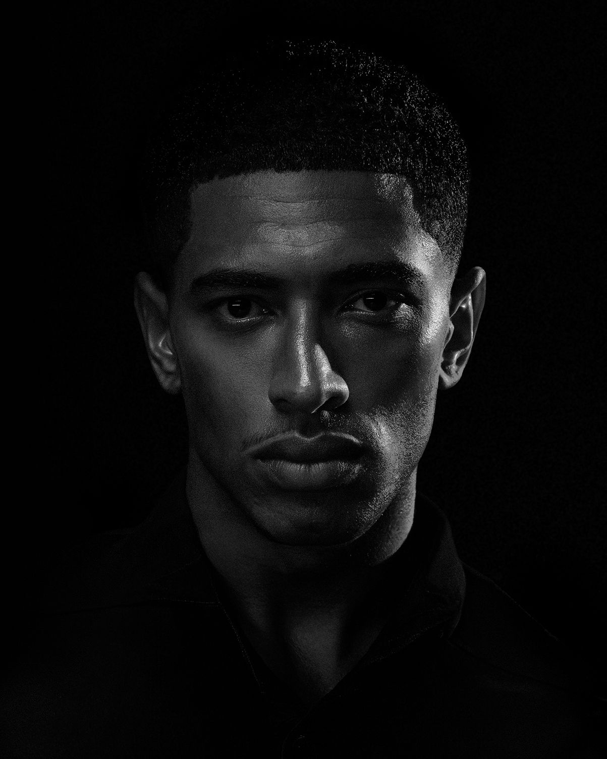 Dramatic black and white portrait photograph with strong contrast and moody lighting against dark background.