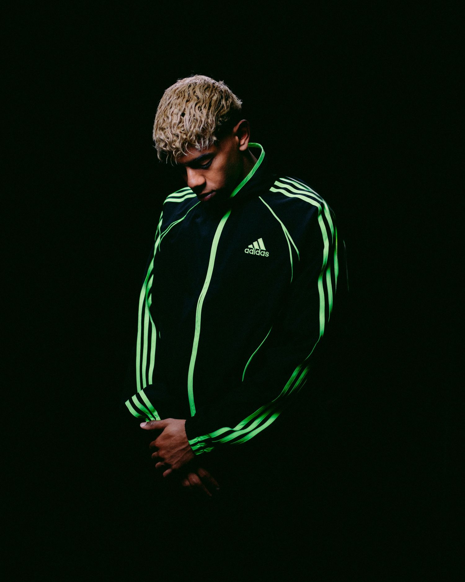 Person in Adidas jacket photographed in dramatic low-key lighting against dark background.