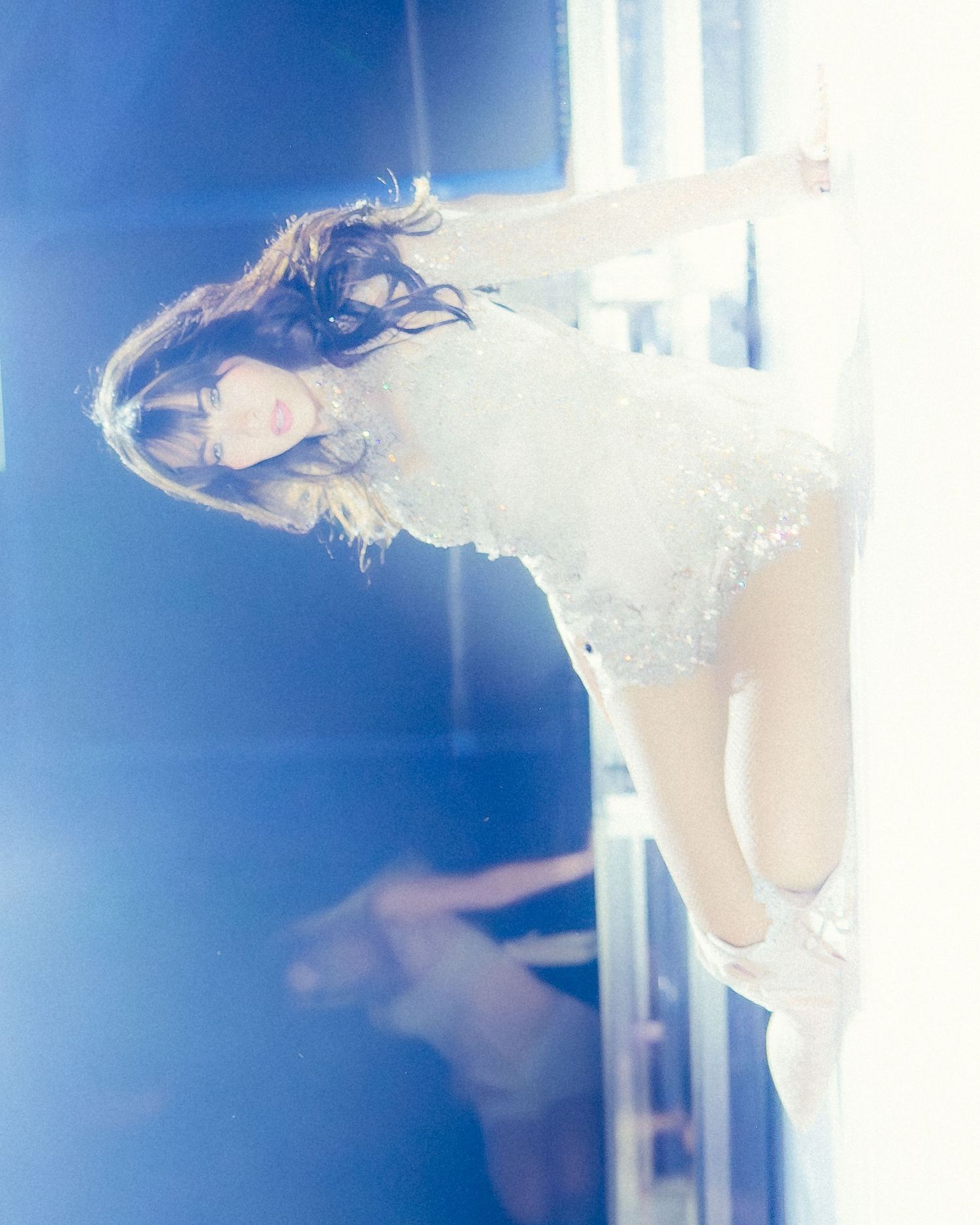 A woman in a white lace dress poses dynamically in bright blue-tinted light, hair flowing.