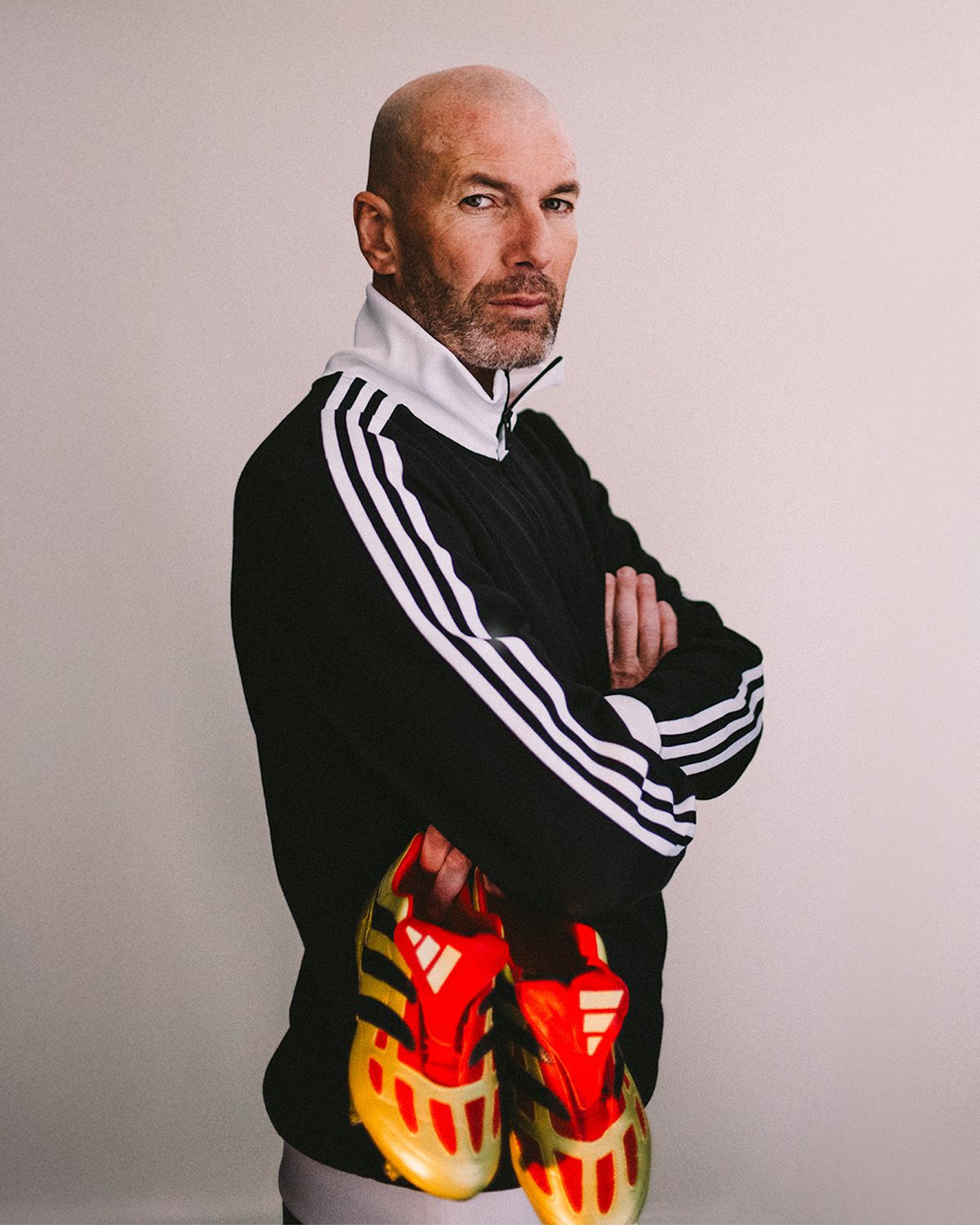 Person wearing black Adidas track jacket posing with bright red and yellow sneakers.