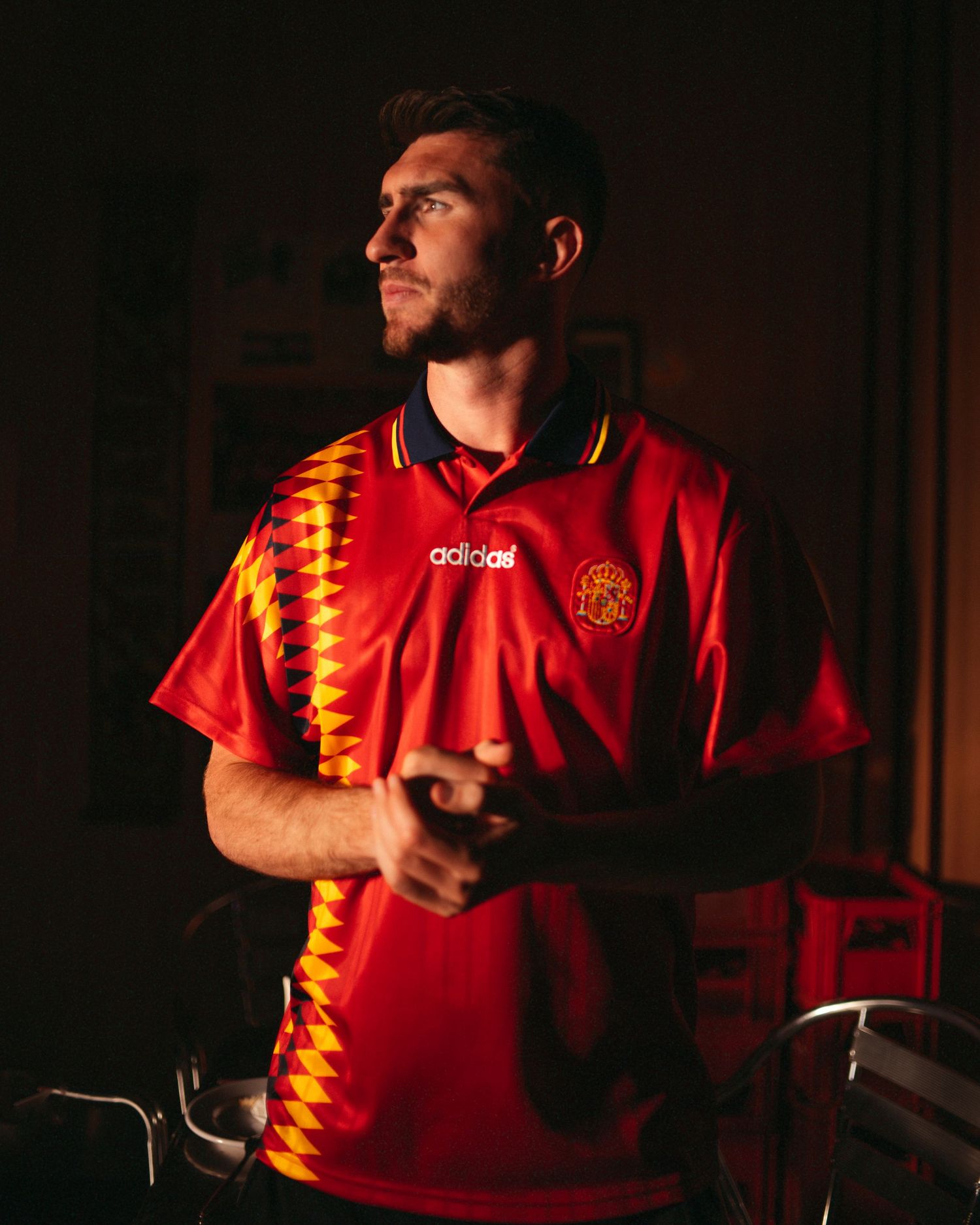 Man wearing a red Adidas Spain retro football shirt with gold geometric pattern details and navy collar.