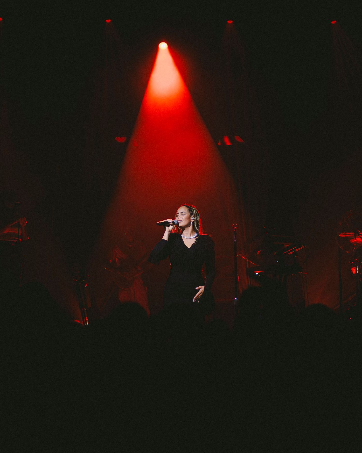 Concert performer singing on stage illuminated by dramatic red spotlight in dark atmospheric setting.
