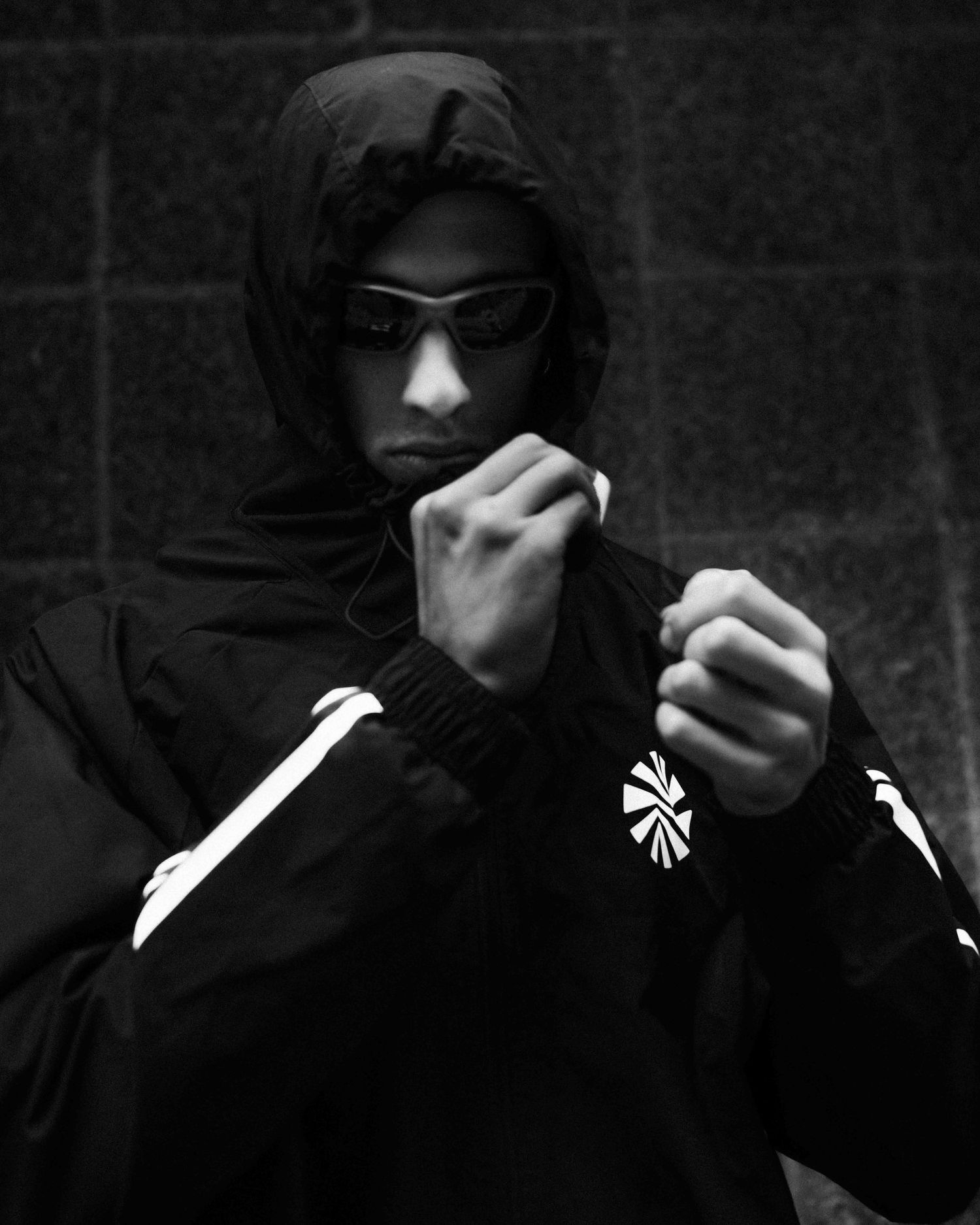 Black and white photo of a person in a hooded jacket and sunglasses posing with raised fists in a fighting stance.