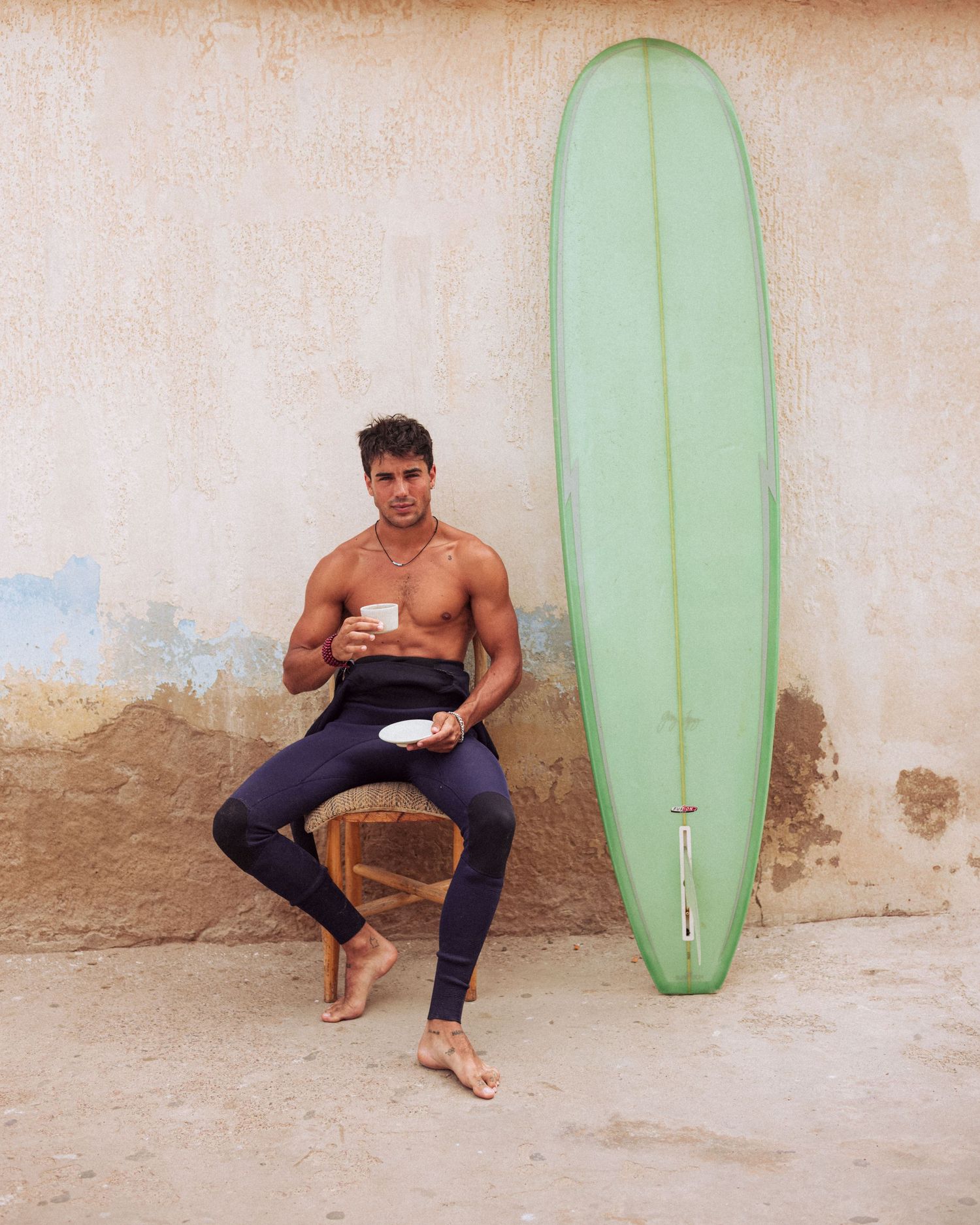 Surfboard leaning against a weathered wall with beachwear and casual poses.