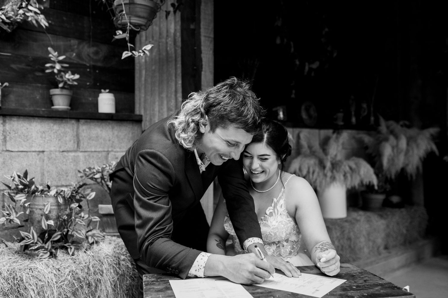A couple signs documents together in an intimate black and white moment on their wedding day.