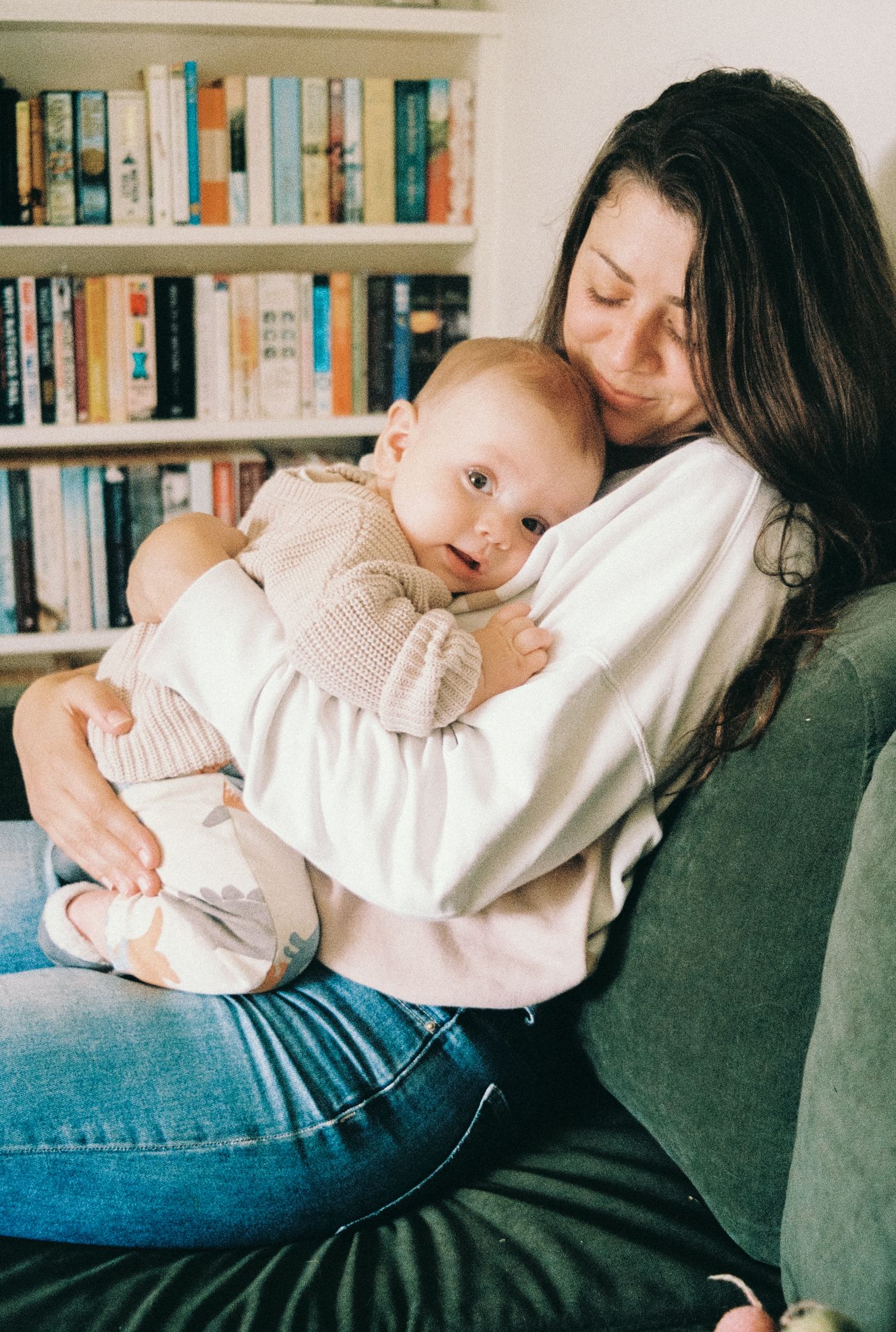 A series of tender parenting moments on a couch with bookshelves in the background.