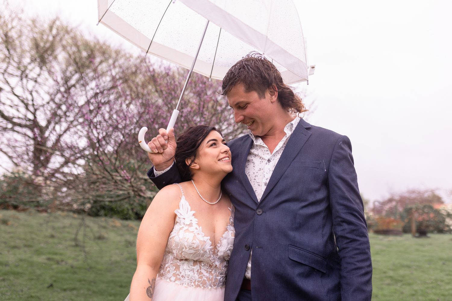 A candid wedding moment captured with the couple sharing an umbrella in a spring garden setting.