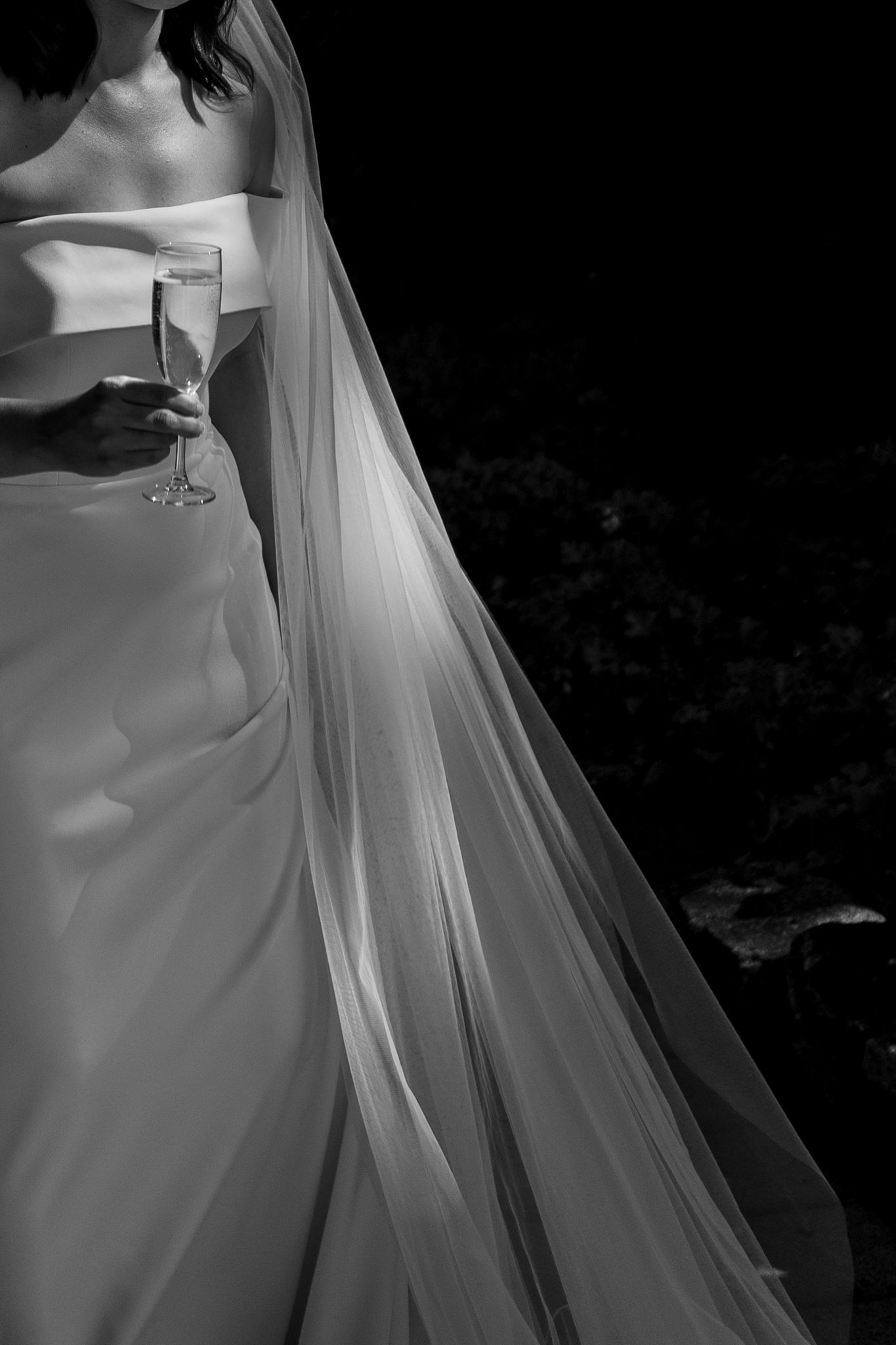 Black and white detail shot of a wedding dress and veil with a champagne glass.