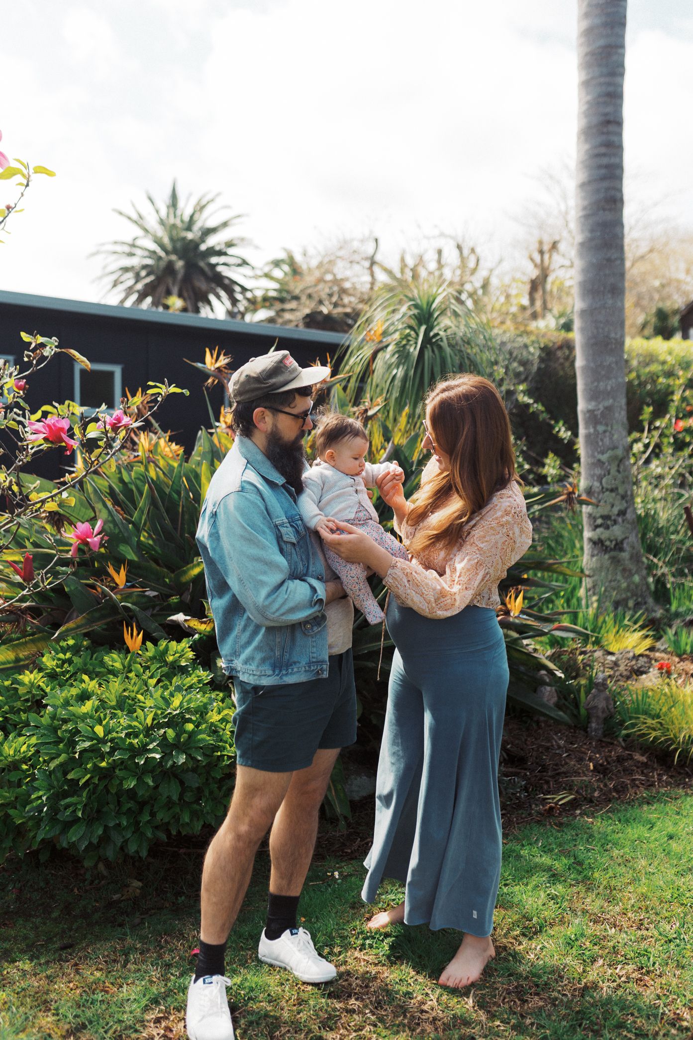 A couple embraces in a lush tropical garden with palm trees and colorful flowers in the background.
