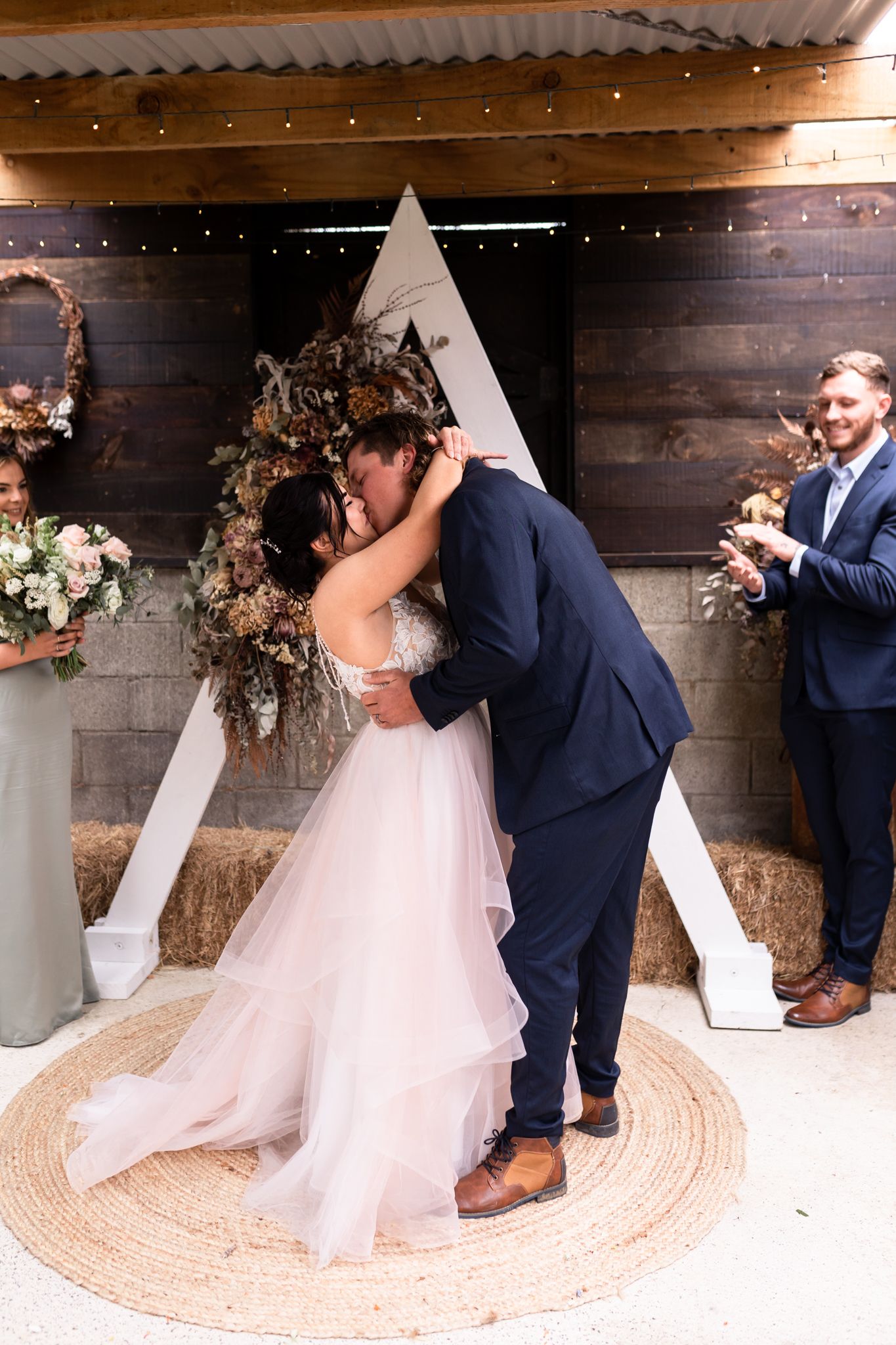 Romantic wedding kiss in front of a geometric white backdrop with floral decorations.