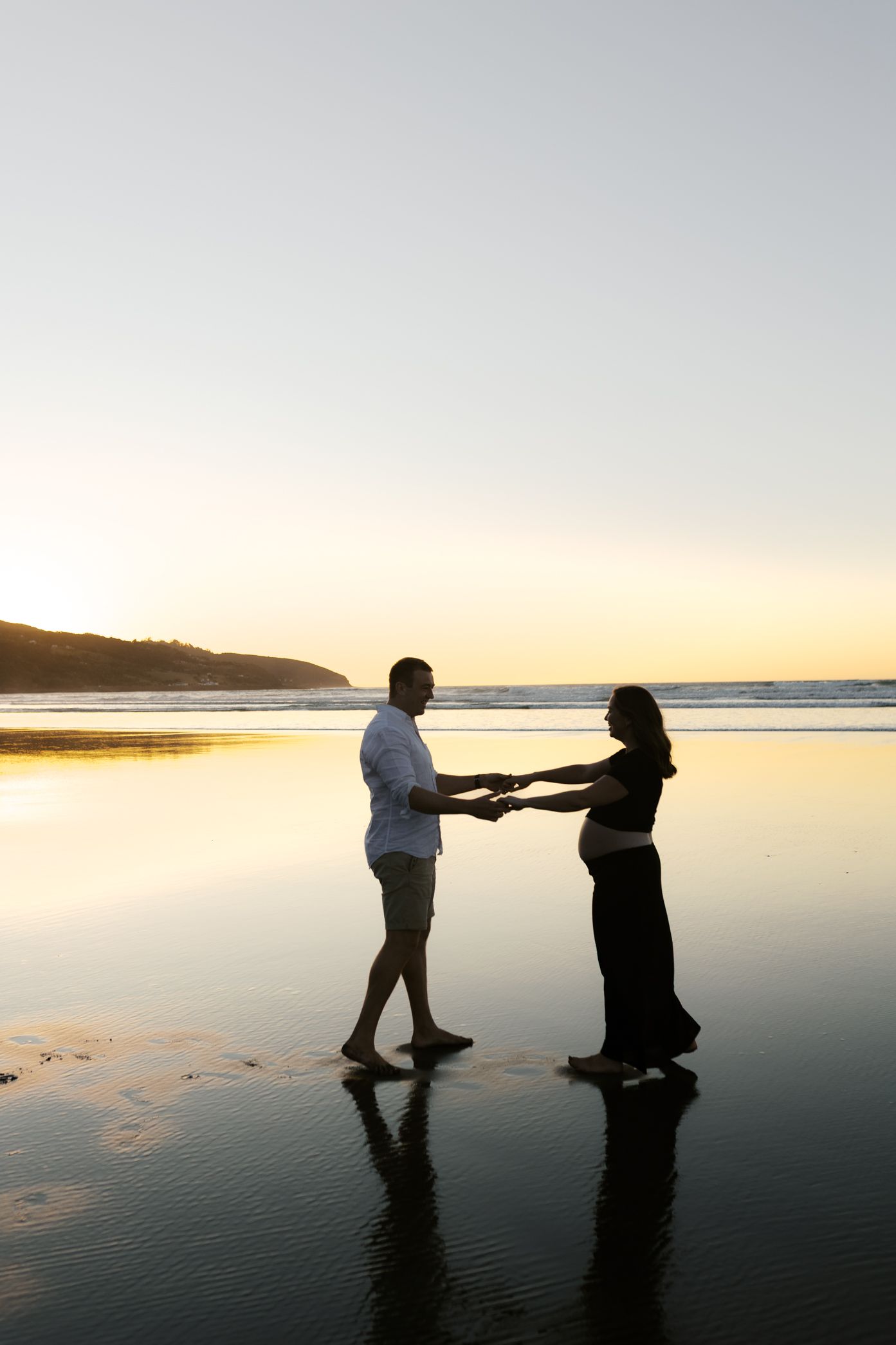 Silhouetted couple on beach at sunset during romantic proposal moment.
