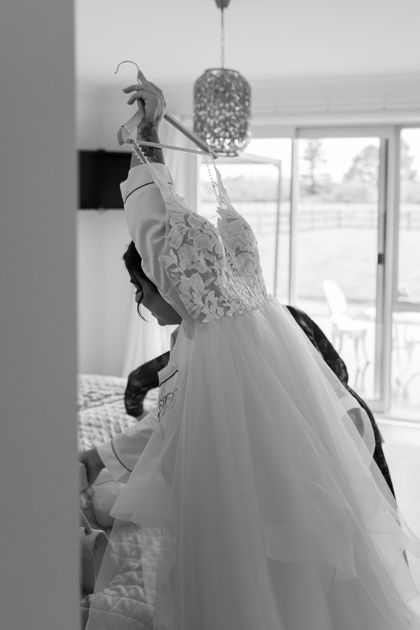 A white lace wedding dress hanging on display with a decorative chandelier in the background.