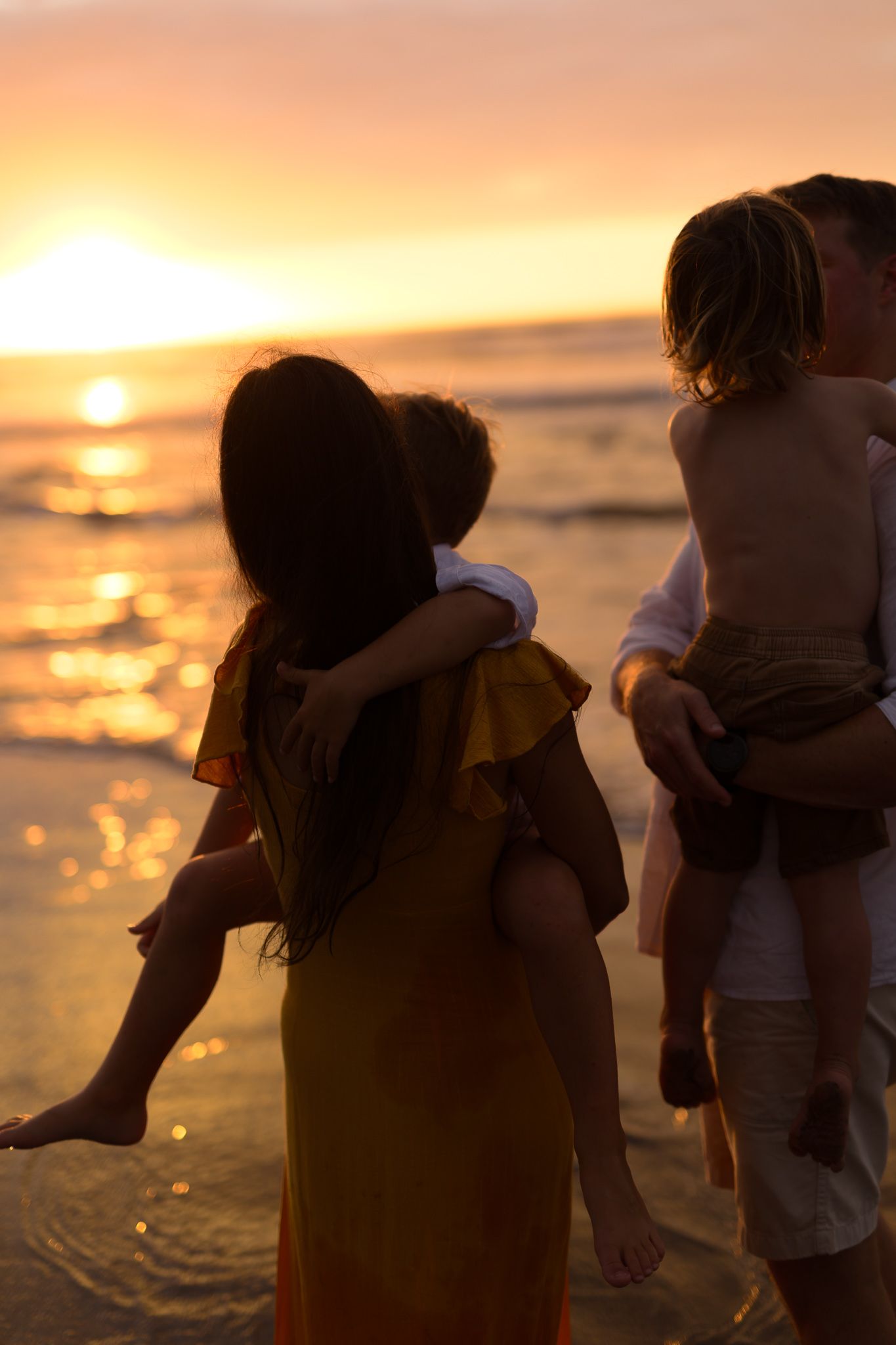 Silhouetted couple embracing on beach during golden sunset with waves reflecting orange light on shoreline.