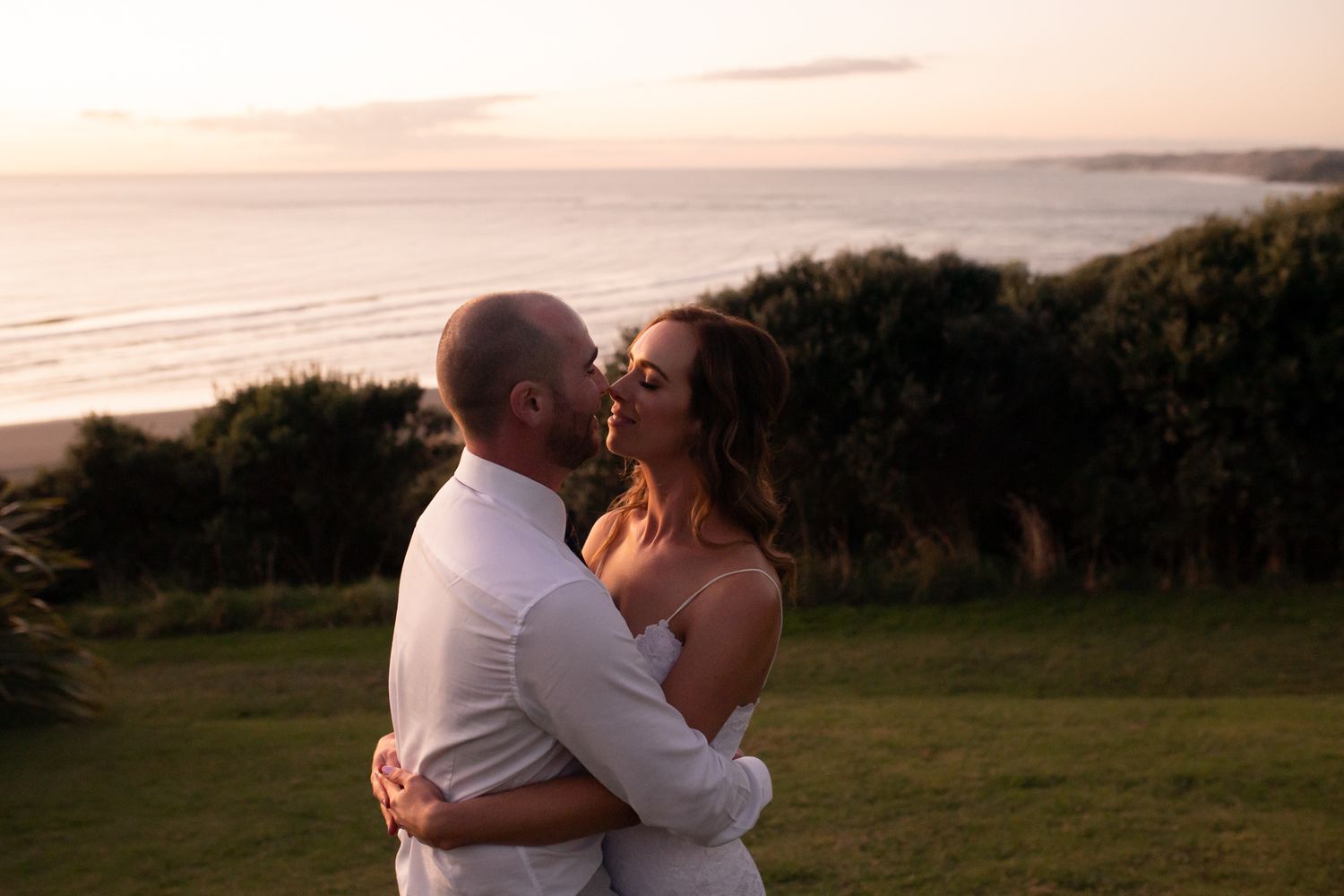 A couple shares an intimate moment at sunset on a coastal cliff overlooking the ocean.
