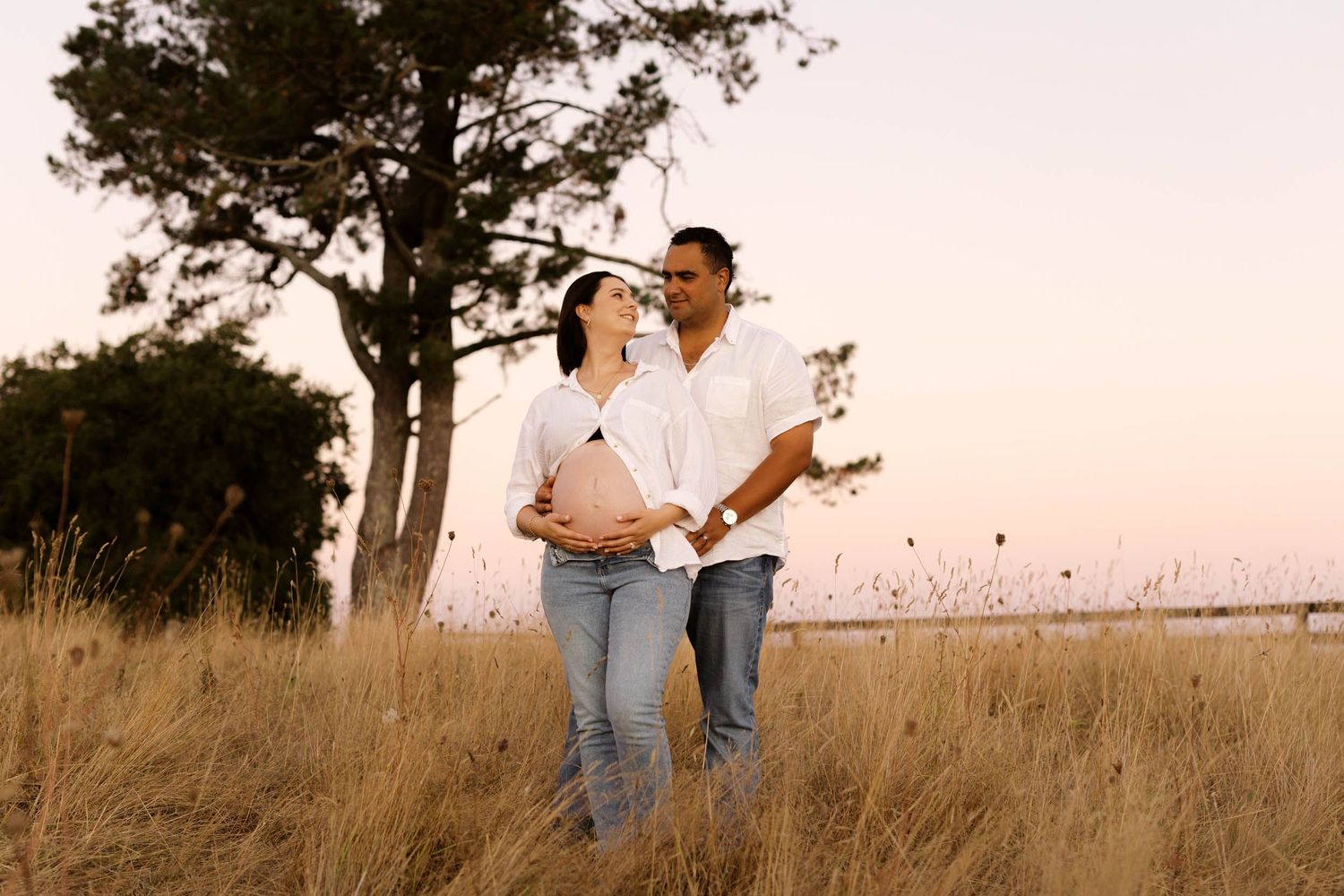A couple embraces romantically in a golden field of tall grass during sunset.