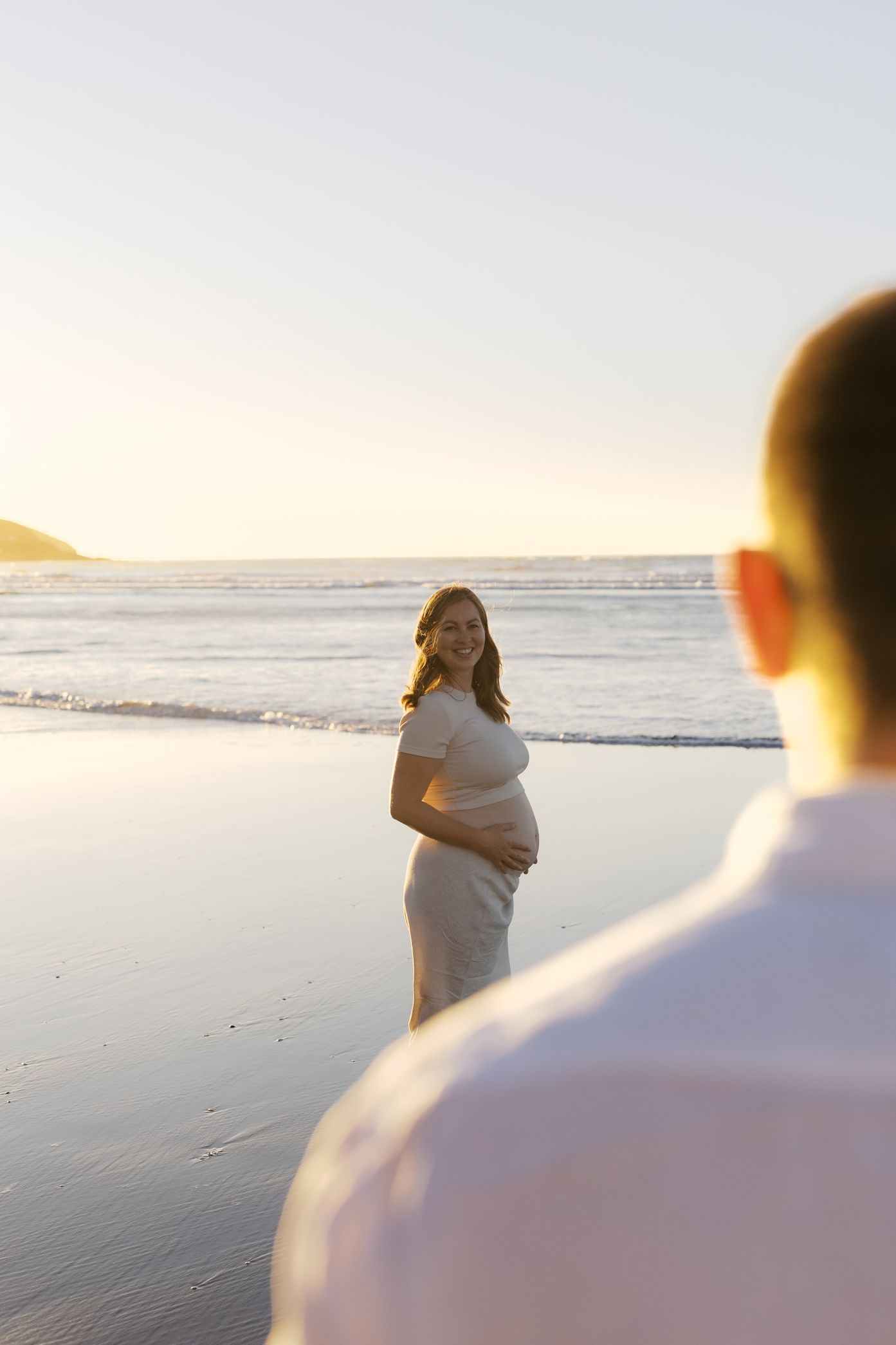 A sun-filled romantic beach scene with people in white clothing walking and enjoying the seaside at sunset.