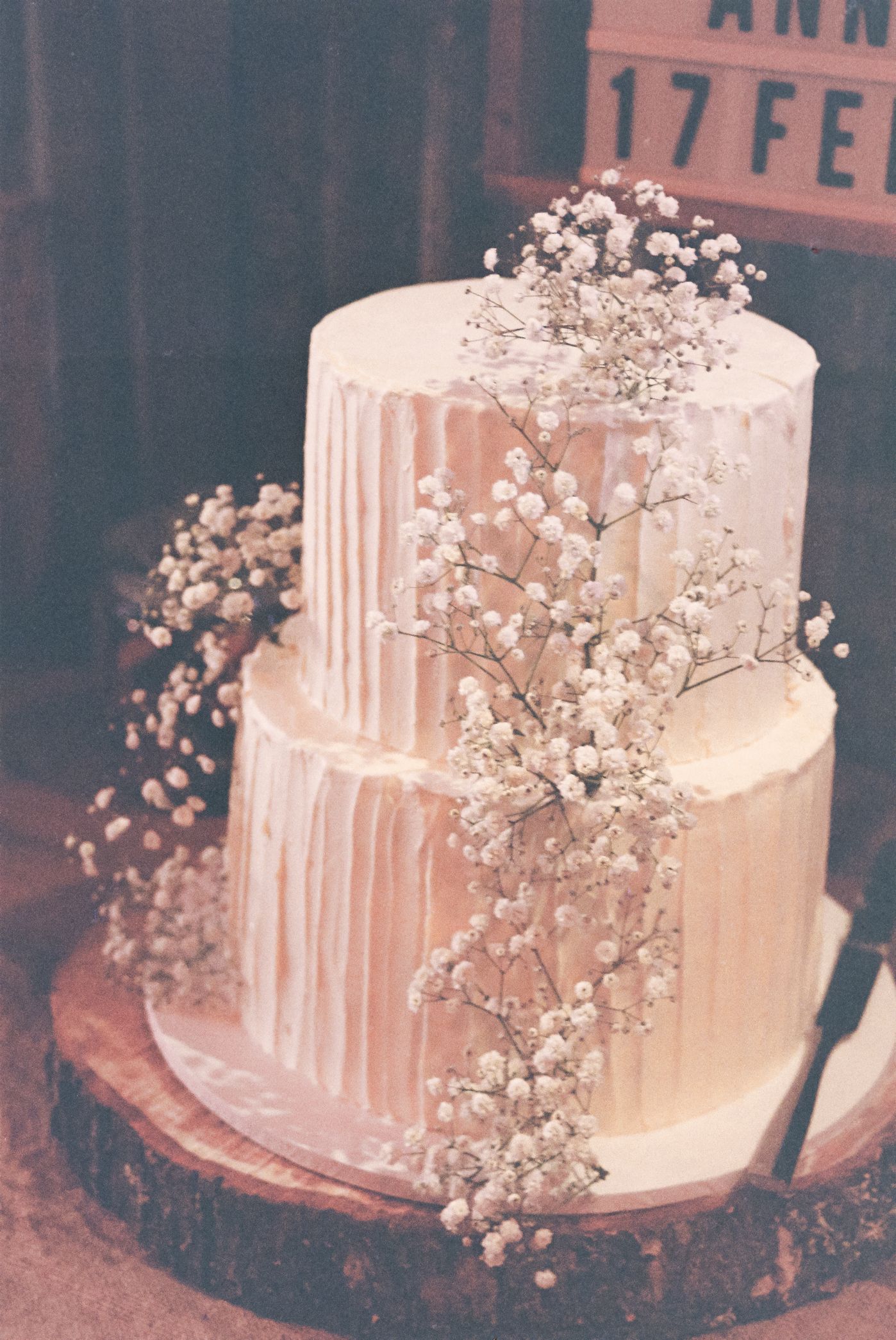 A white wedding cake with dripping icing and delicate baby's breath flowers decorating the tiers.