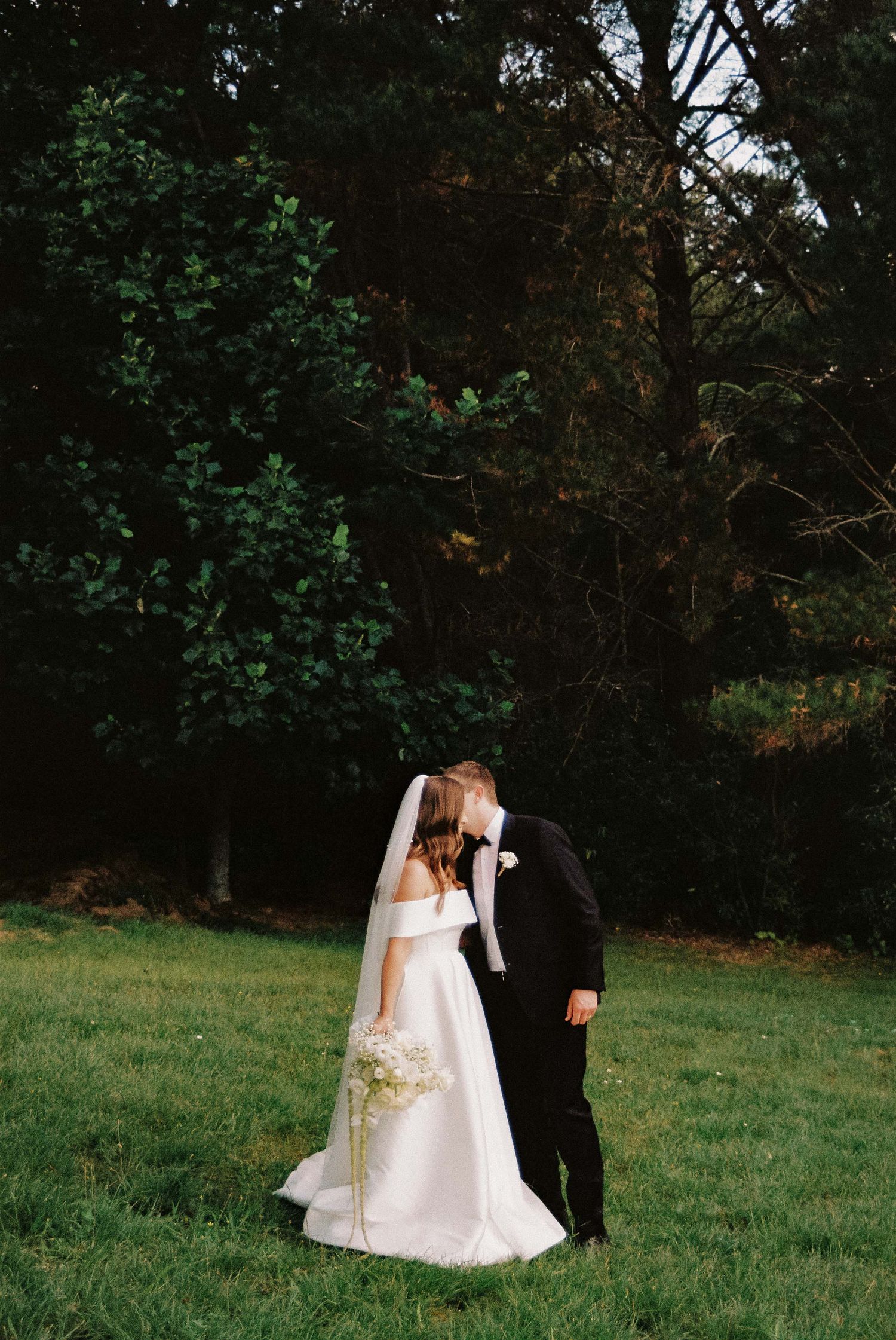 Bride and groom share an intimate moment on their wedding day in a garden setting.