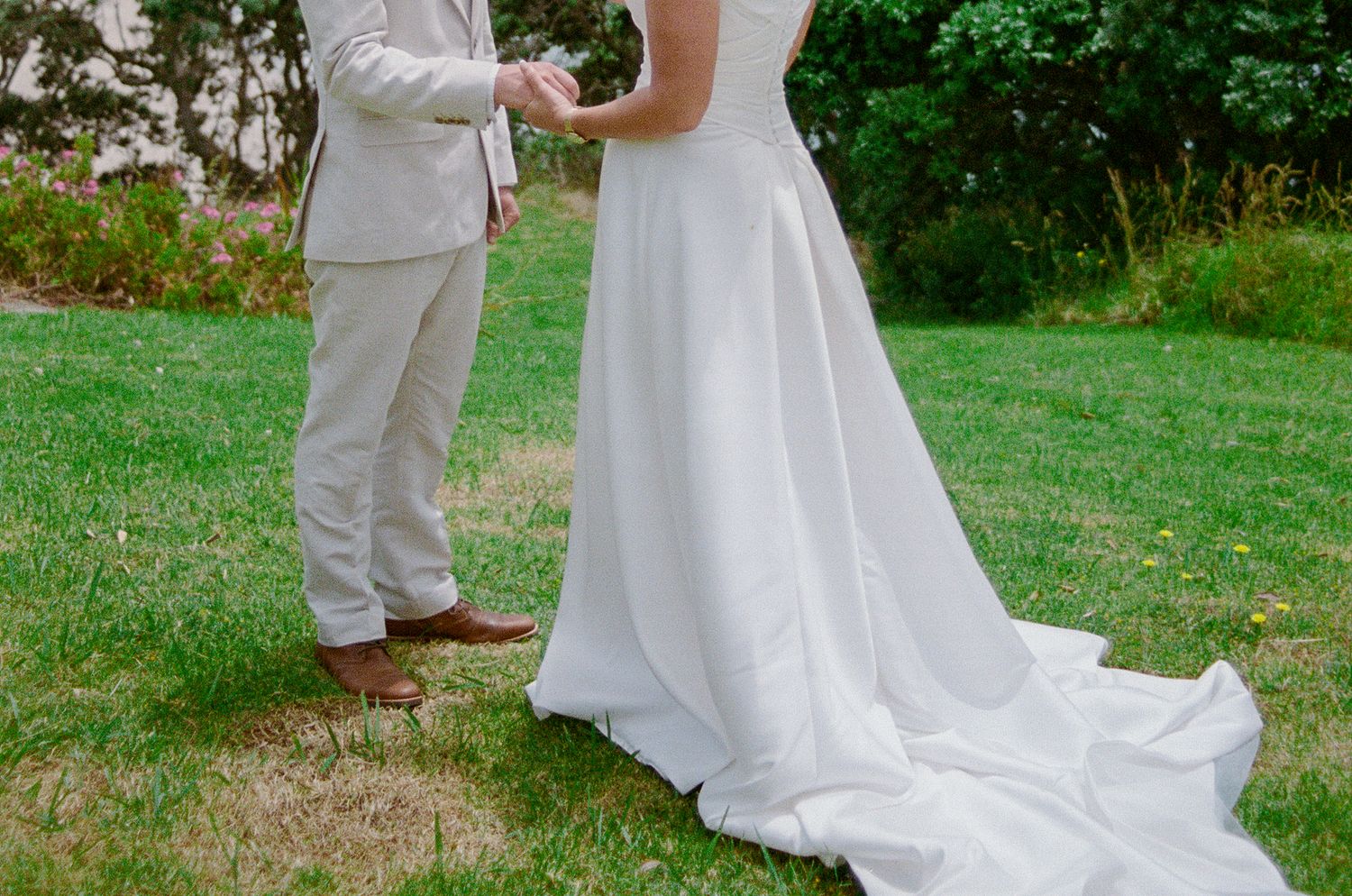 A couple in wedding attire shares a tender moment together on a lush green lawn during their outdoor ceremony.