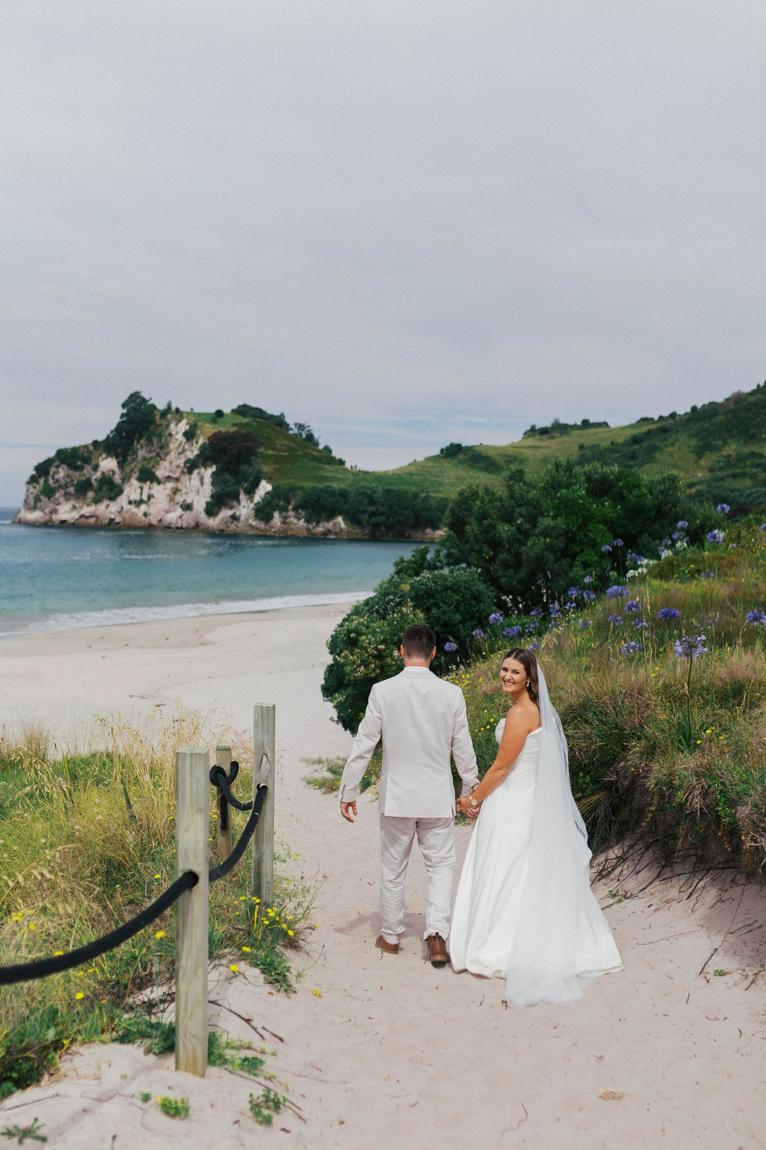 A couple walks along a scenic coastal path with white cliffs and turquoise waters at a secluded beach cove.
