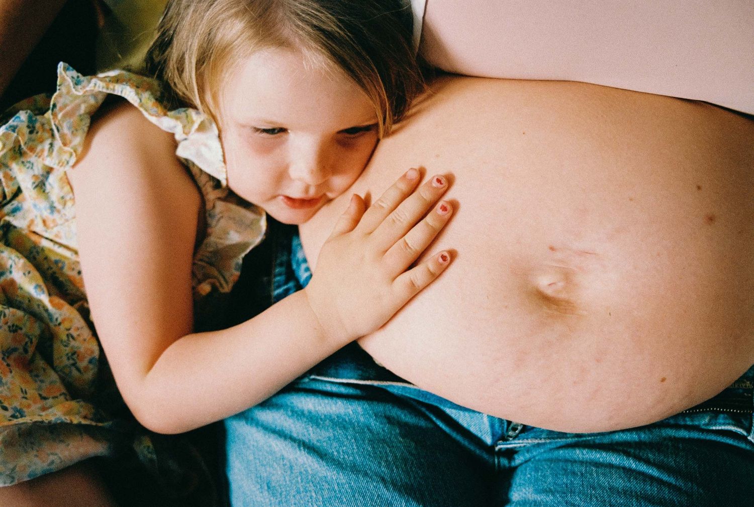 A child gently places their hand on a pregnant belly while laying down together in a tender moment. Experienced family photographer.