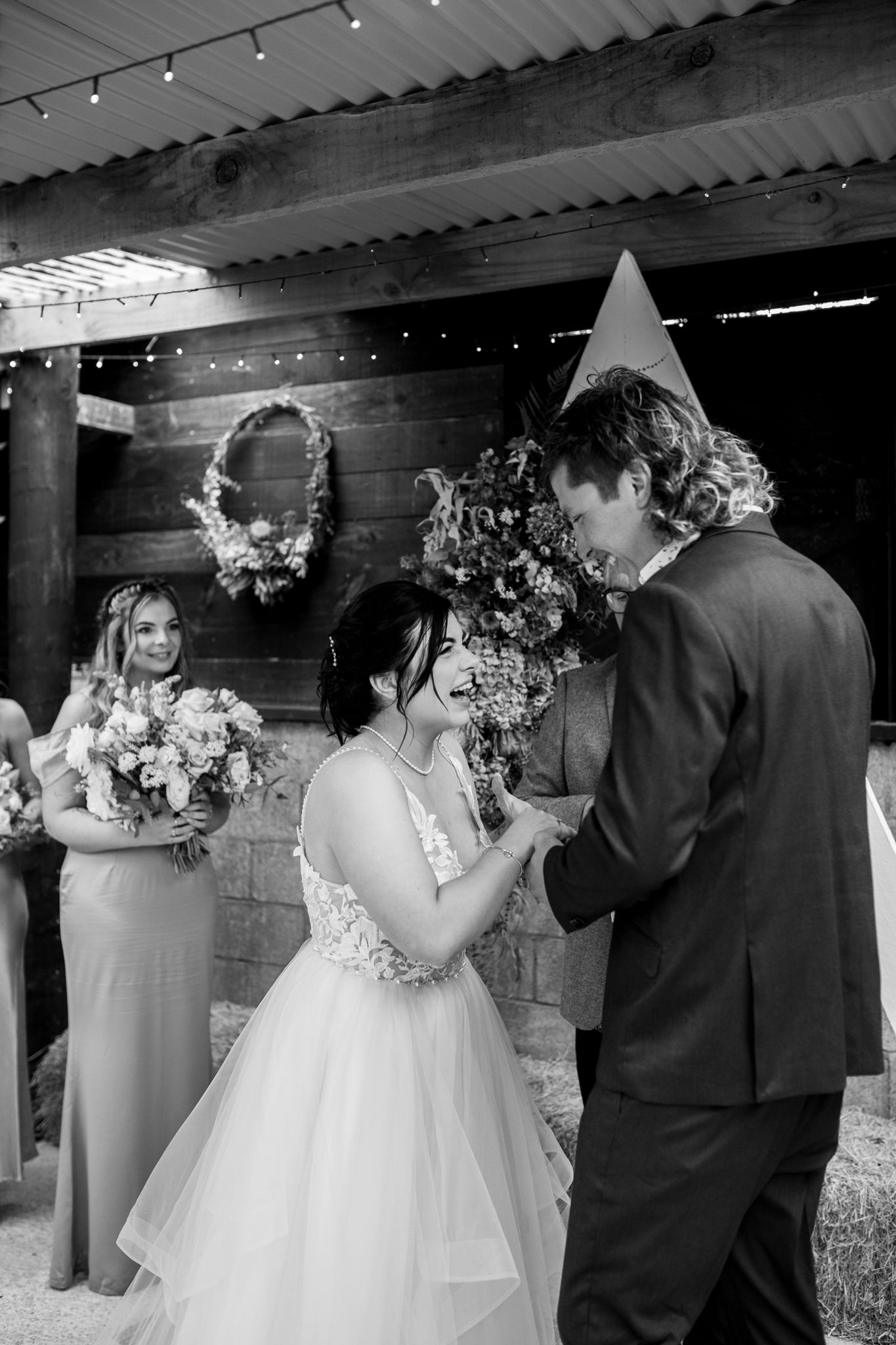 Intimate wedding ceremony moment in a rustic barn with string lights and wooden backdrop.