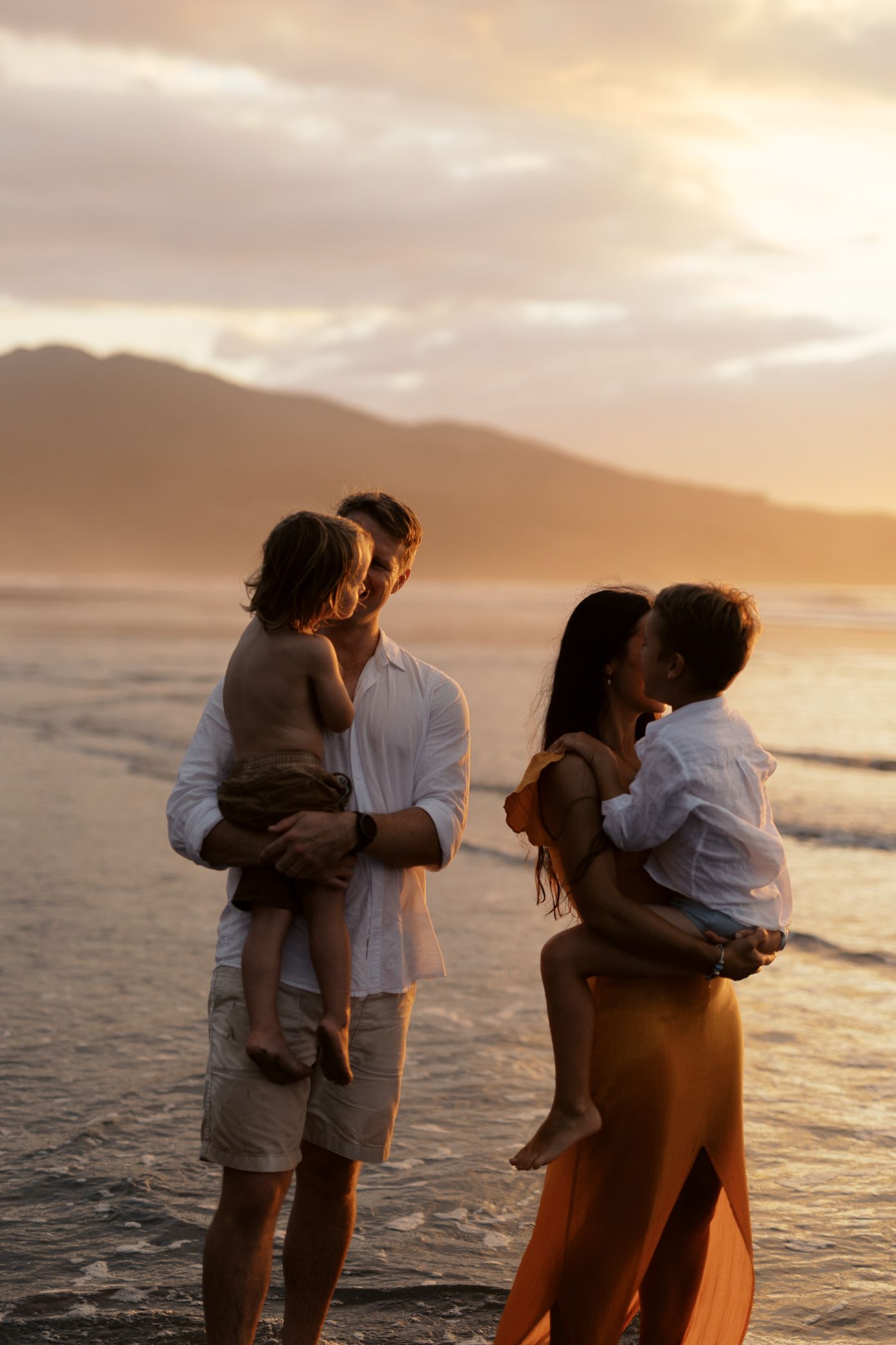 A couple embraces on a beach during sunset casting silhouettes against the golden sky and ocean waves.