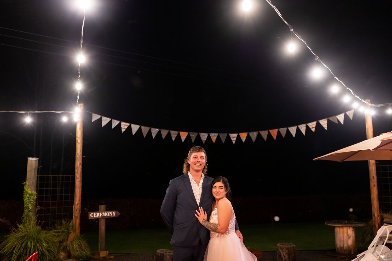 A nighttime wedding portrait under string lights and colorful bunting flags.