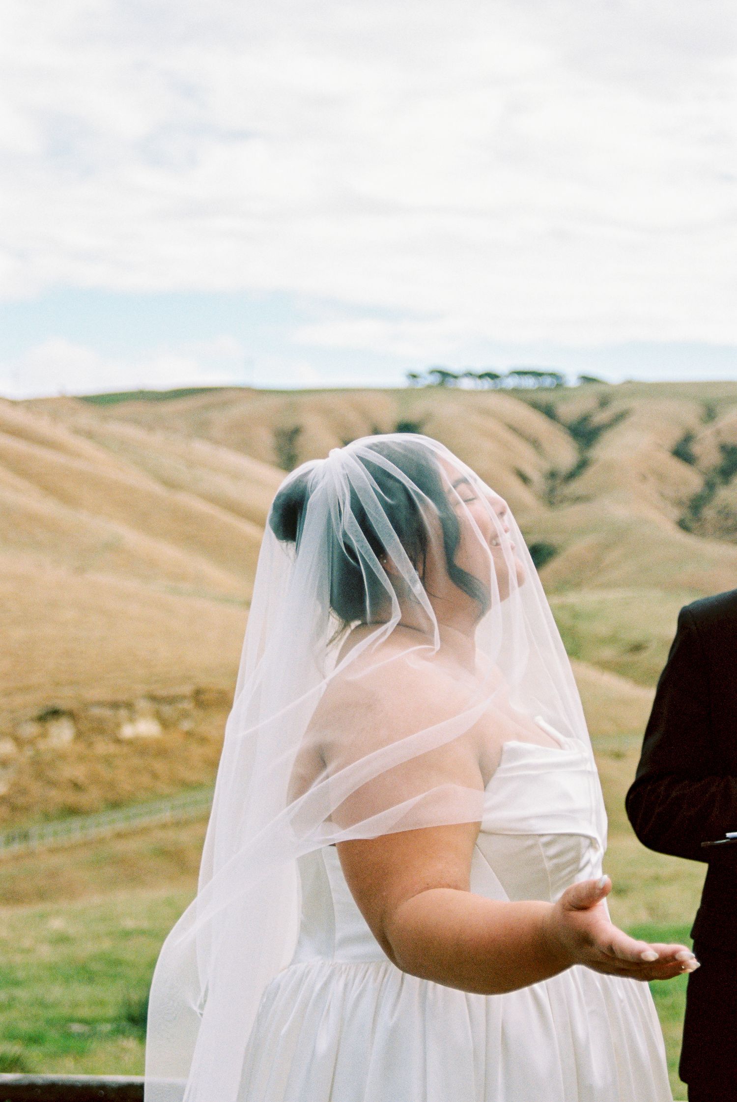 Rolling green hills create a scenic backdrop for a romantic wedding moment under a flowing white veil.
