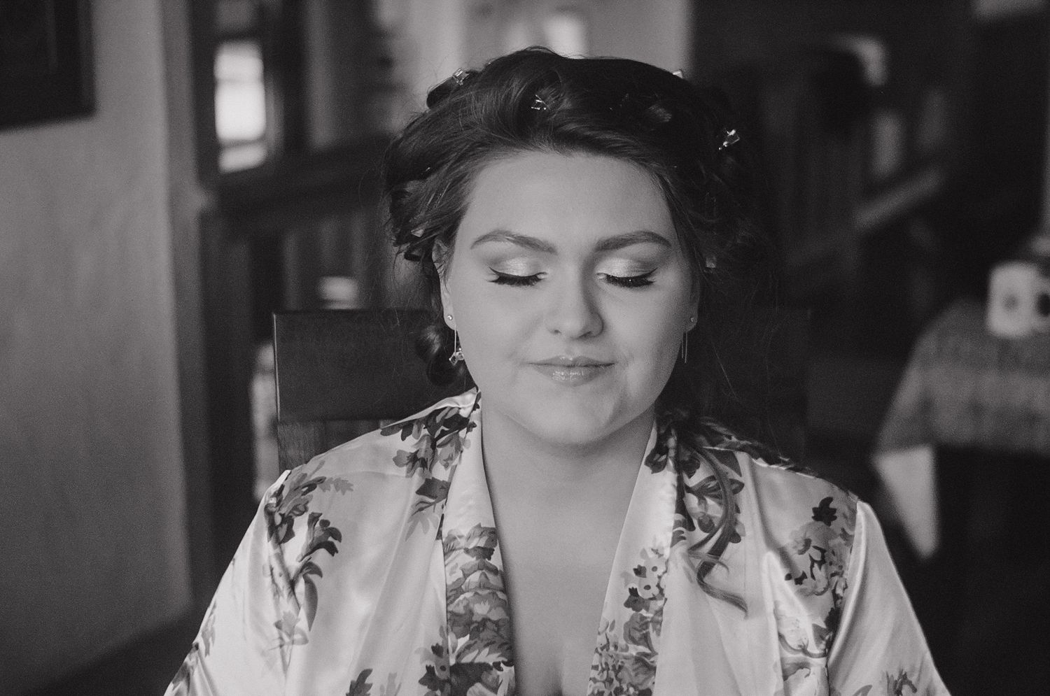 A person wearing a floral dress sits at a desk writing in a notebook in black and white.