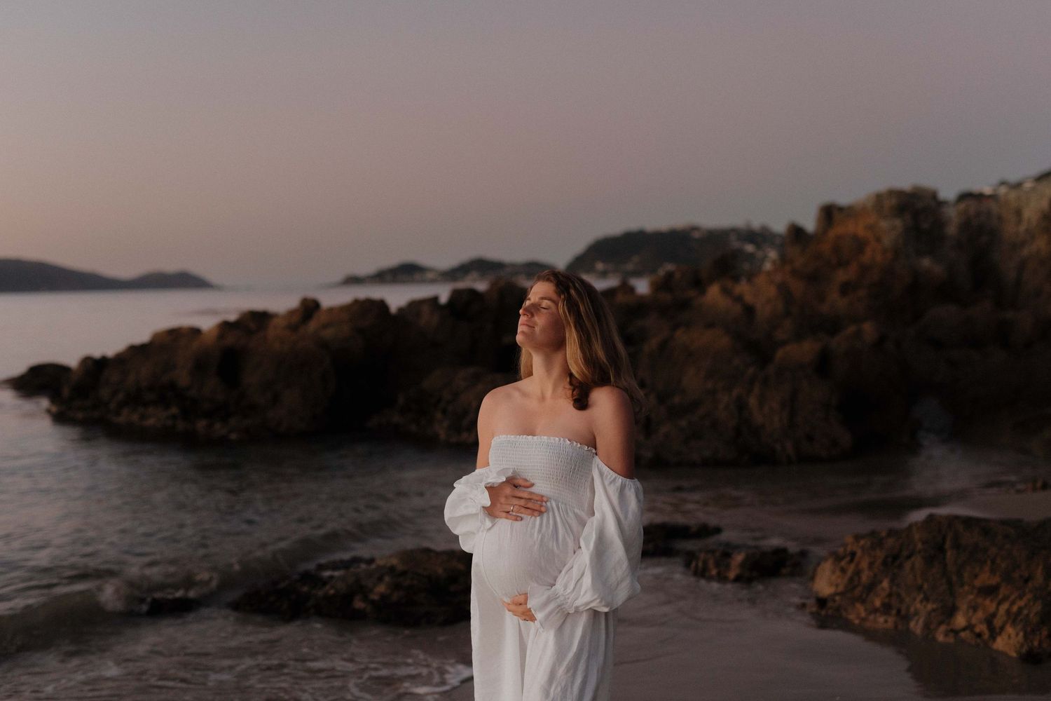 A romantic coastal photoshoot at sunset with rocky cliffs and ocean waves creating a dreamy atmosphere.