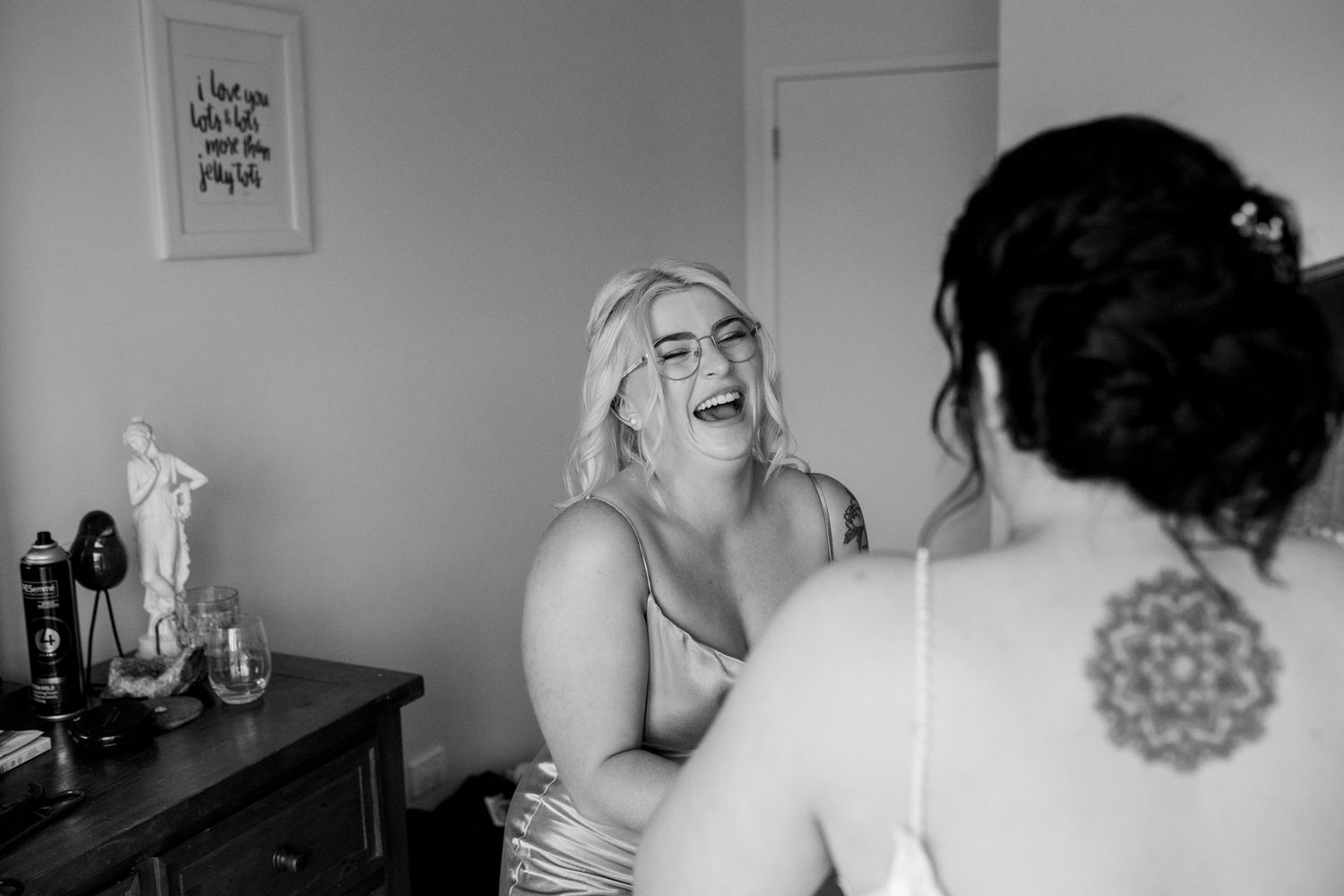 A candid black and white photo capturing joyful laughter during wedding preparations.
