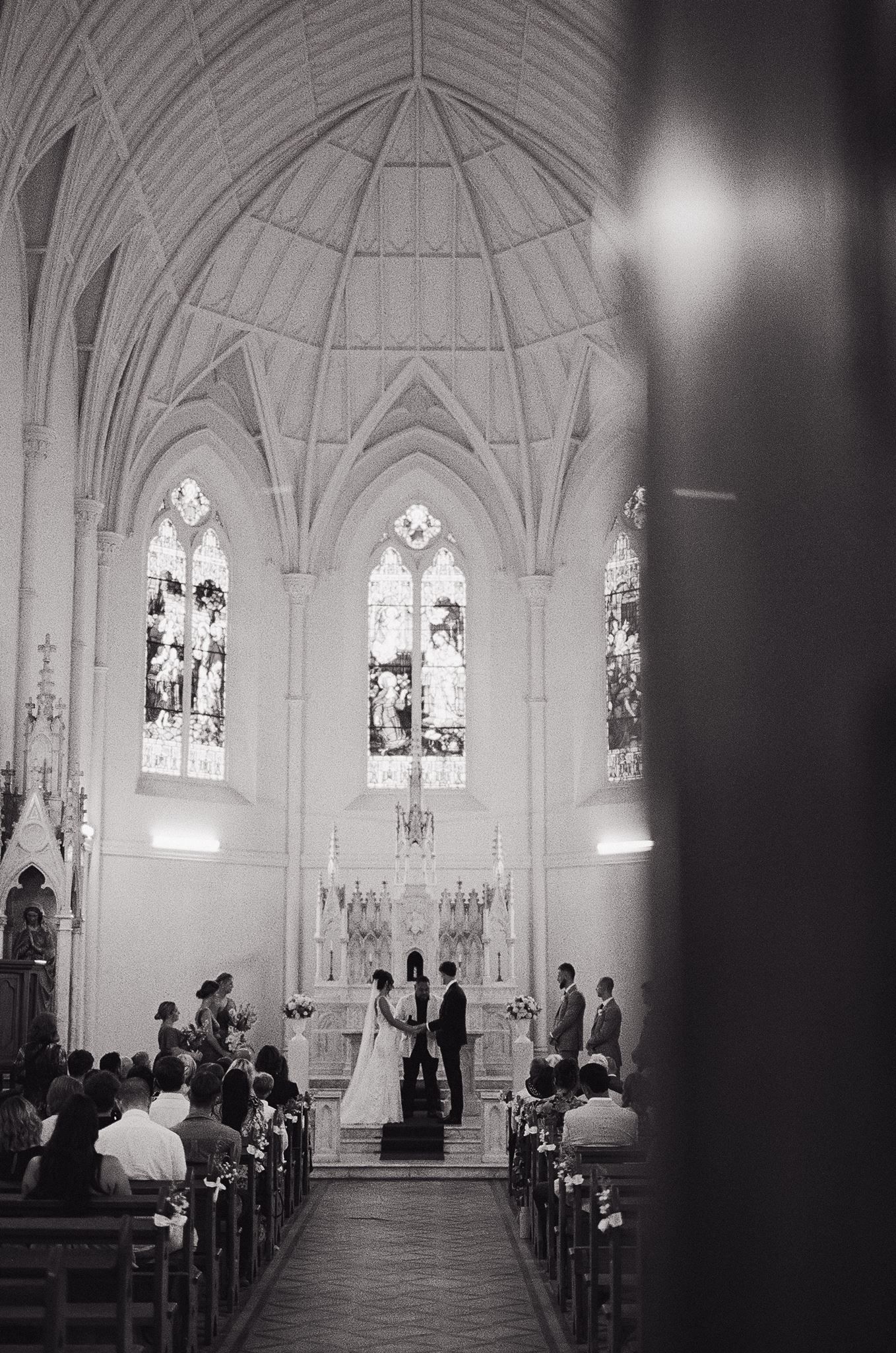 Black and white photo of a wedding ceremony inside a Gothic church with stained glass windows and vaulted ceilings.
