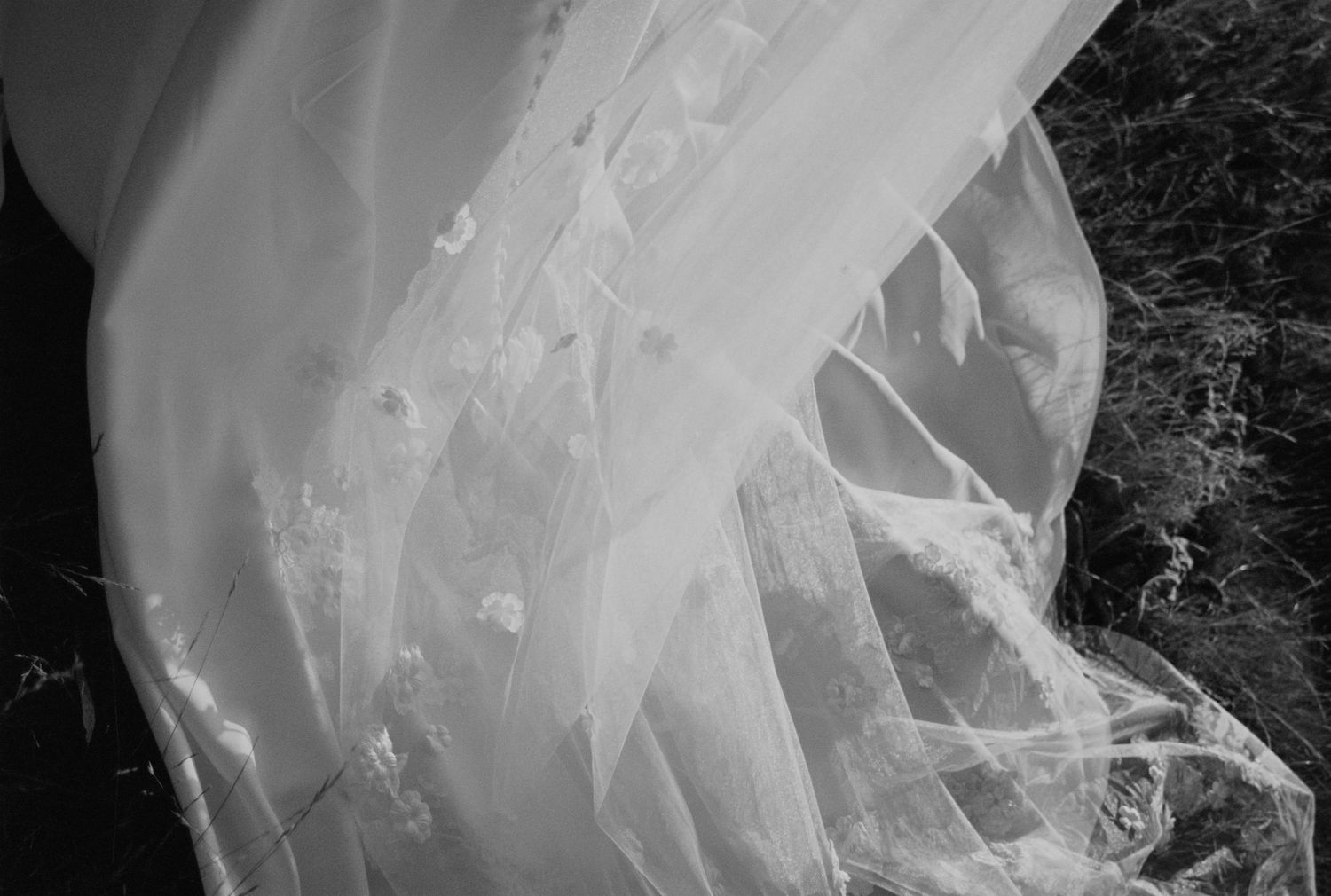 Close-up of delicate white wedding dress fabric with intricate lace details and flowing layers creating elegant texture.