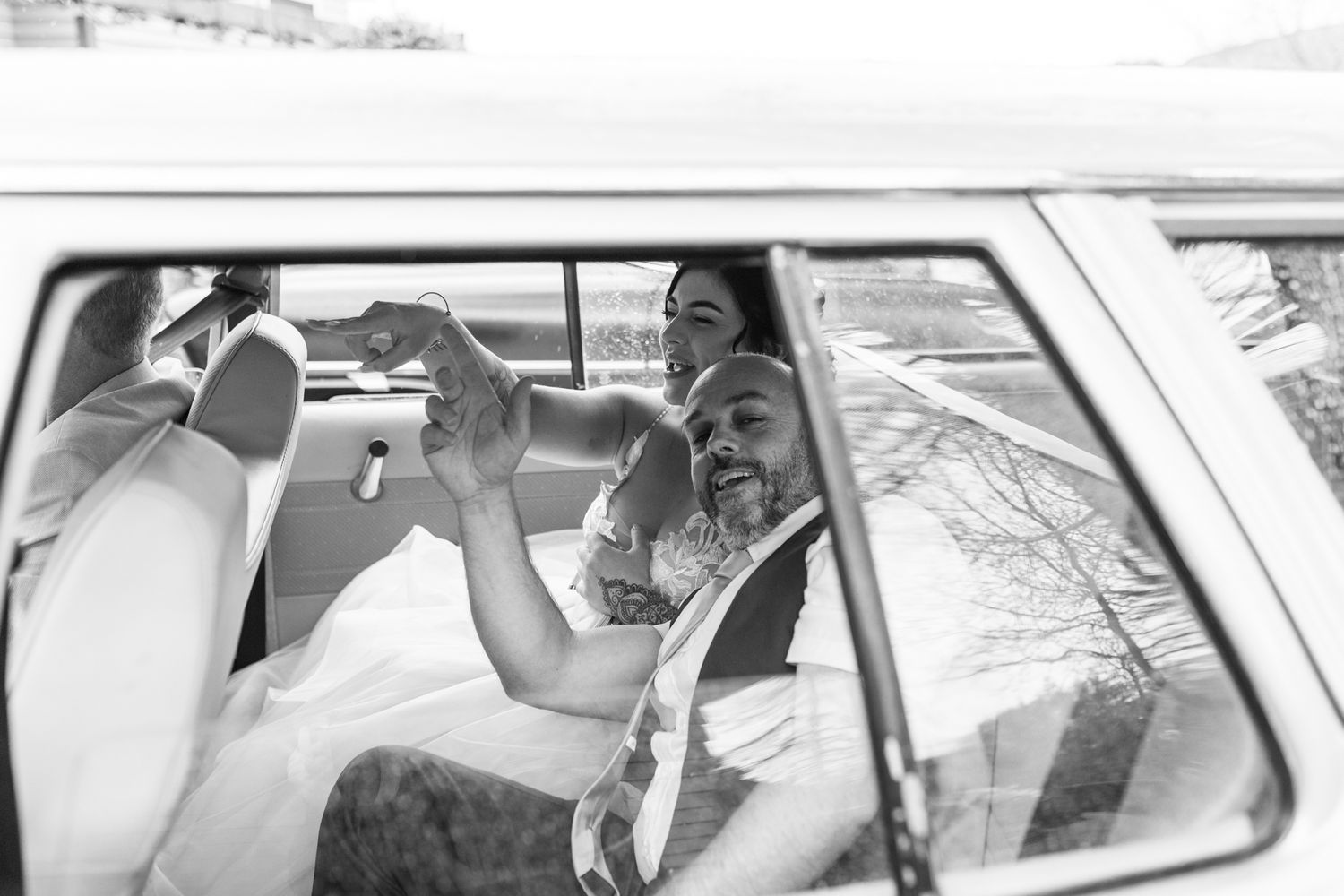 A candid black and white photo captured through a car window on a wedding day.