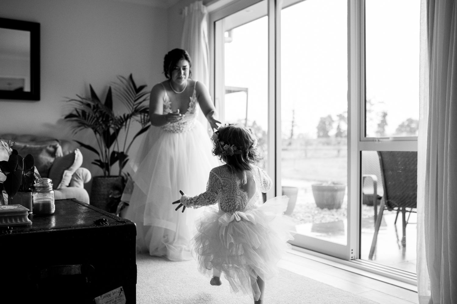 A black and white photo capturing a tender wedding day moment by a bright window.