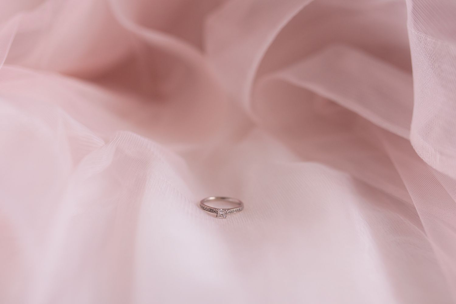 A delicate engagement ring nestled in soft pink tulle fabric.