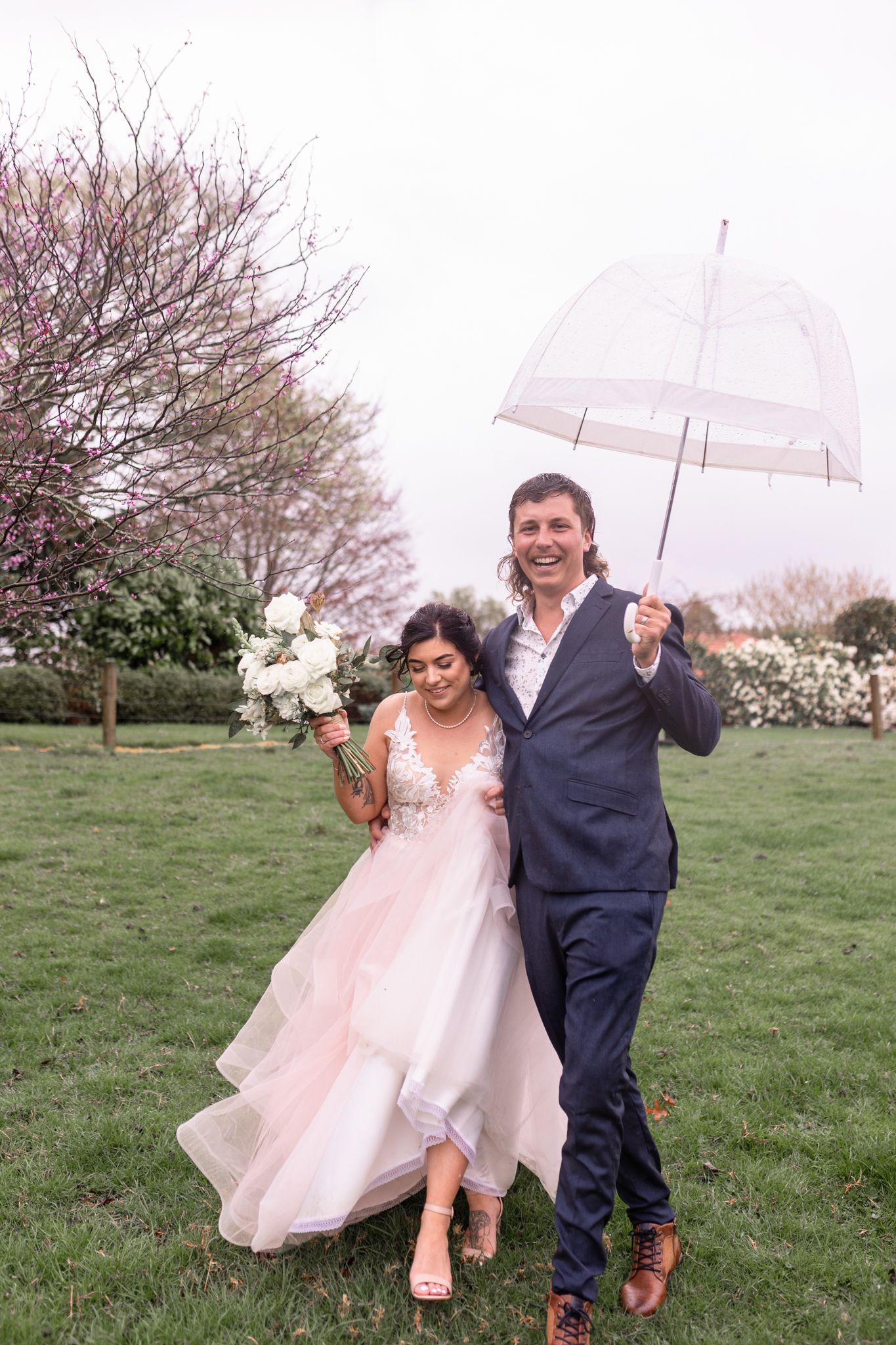 Couple shares romantic moment under clear umbrella in blooming spring garden setting.