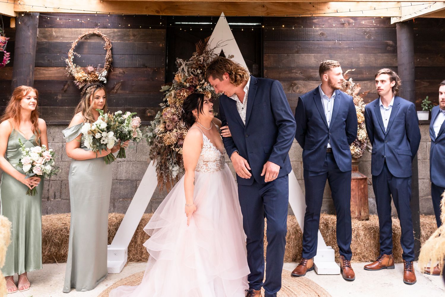 Wedding ceremony in a rustic venue with wooden walls and floral arch decorations.