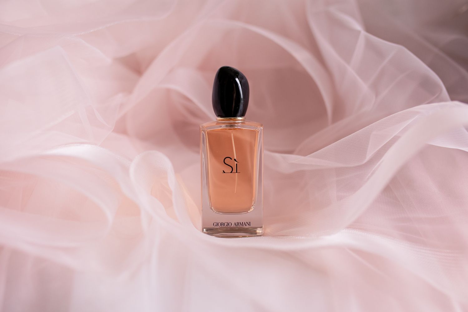 A perfume bottle resting on soft pink tulle fabric with delicate folds.