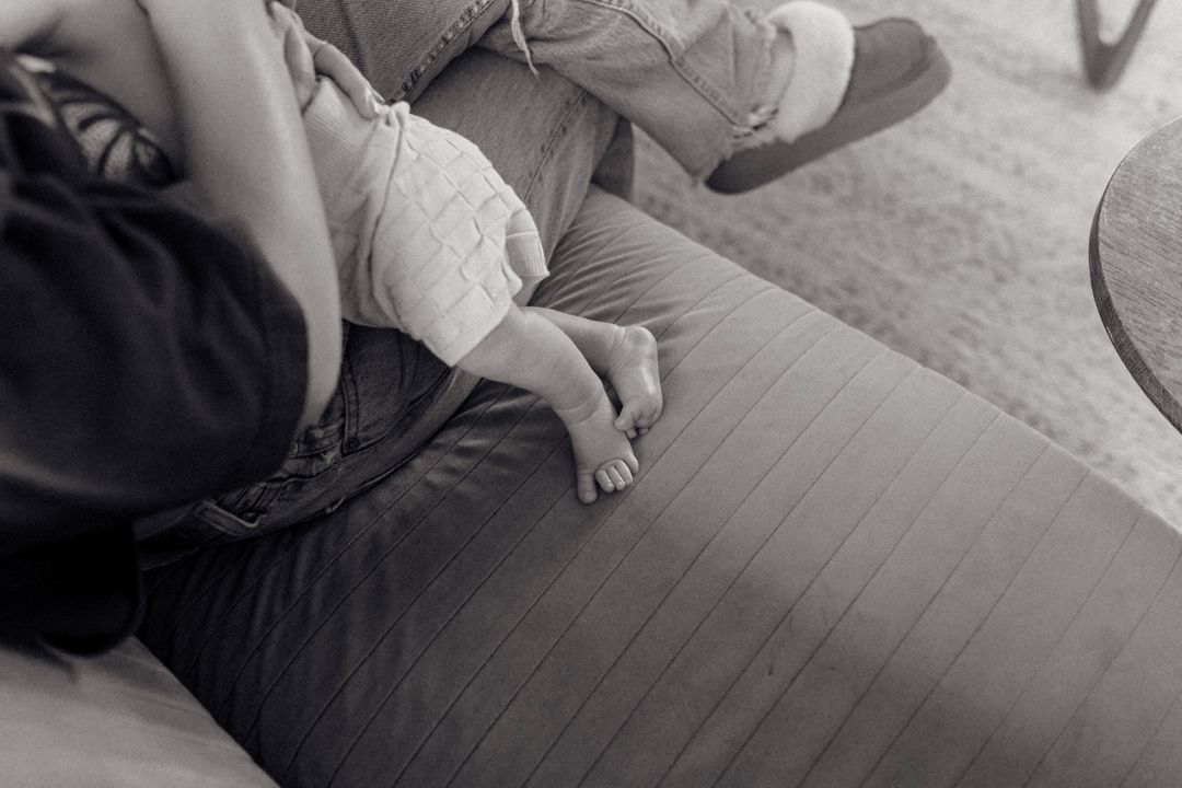 Black and white photo of bare feet resting on a sofa, showing a peaceful and relaxed moment at home. New born photography Wellington.