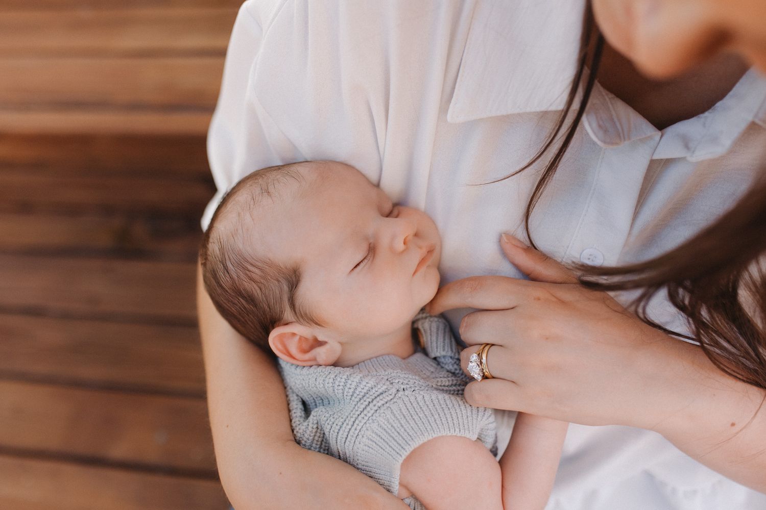 A sleeping newborn baby in a gray onesie rests peacefully in a caregiver's arms.