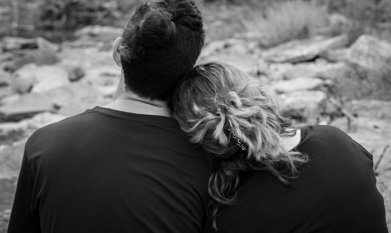 Black and white photo of a couple sitting together, woman resting her head on man's shoulder.