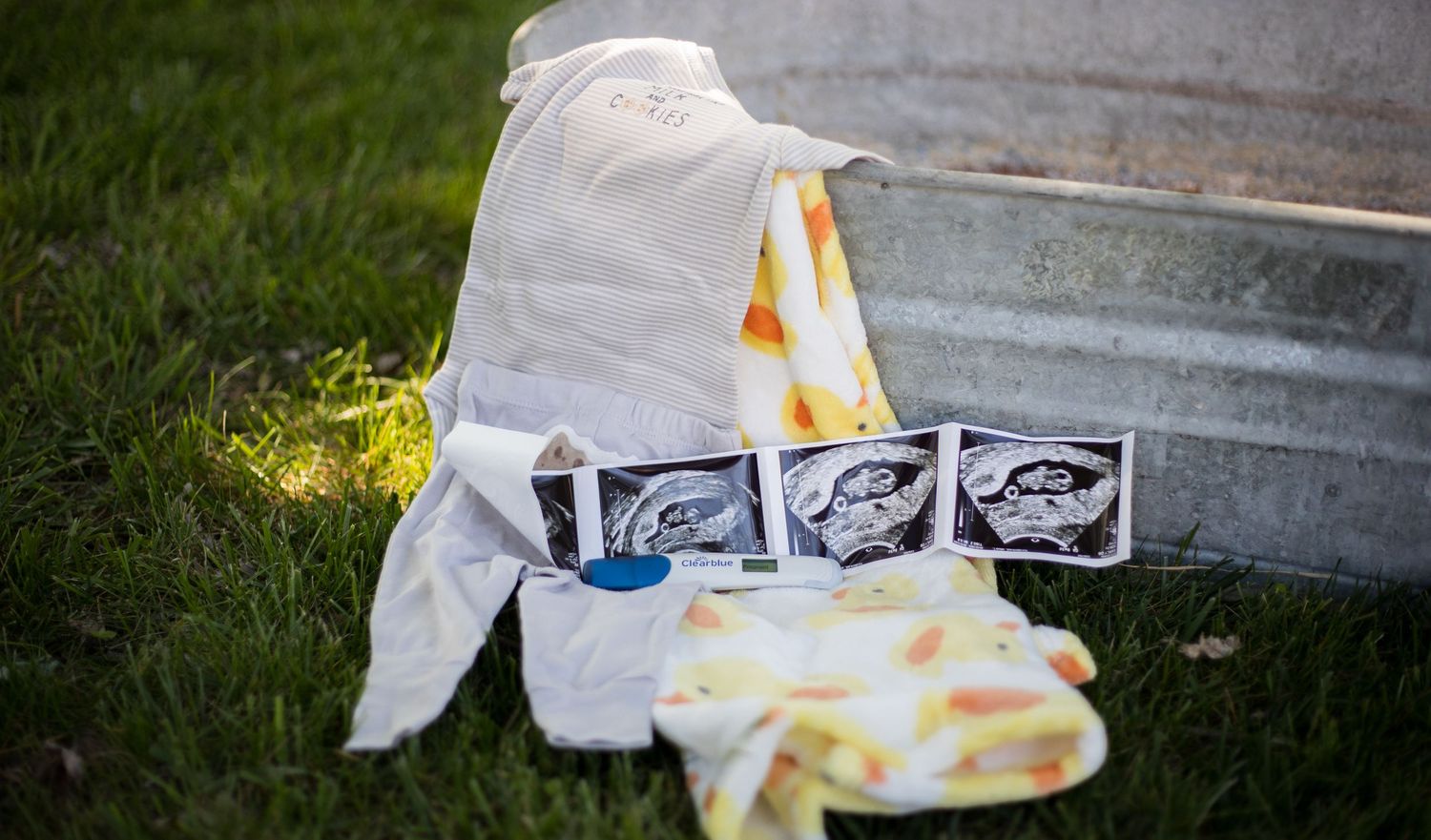 Ultrasound photos and baby items arranged on grass in soft natural light.