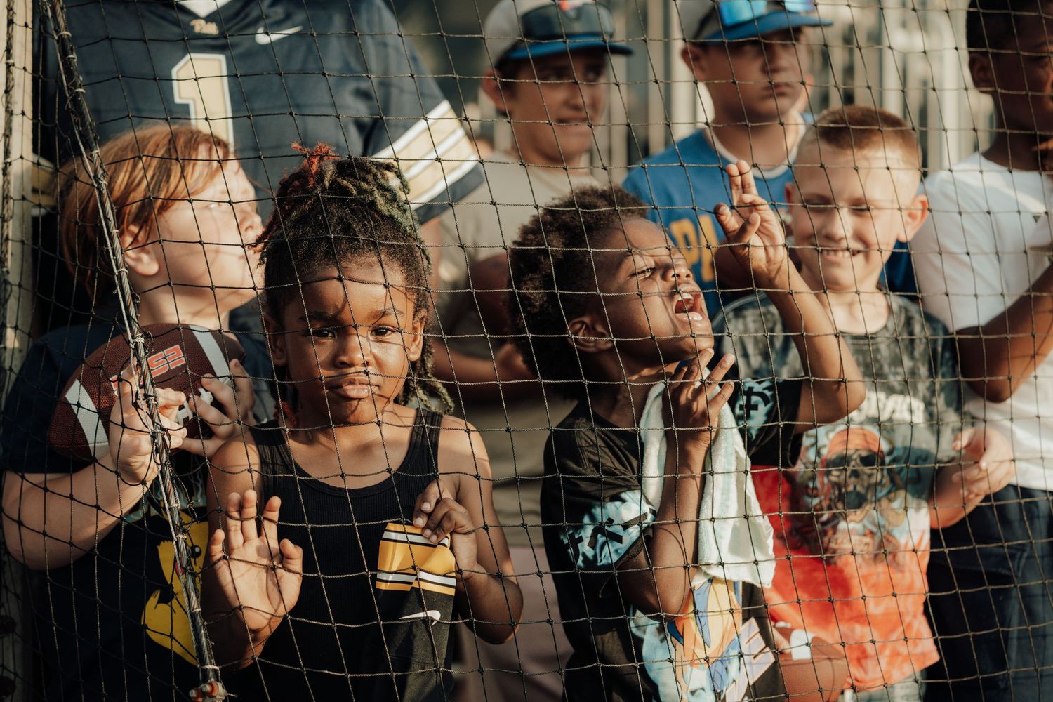 Excited baseball fans watch intently through protective netting at a stadium during a game.